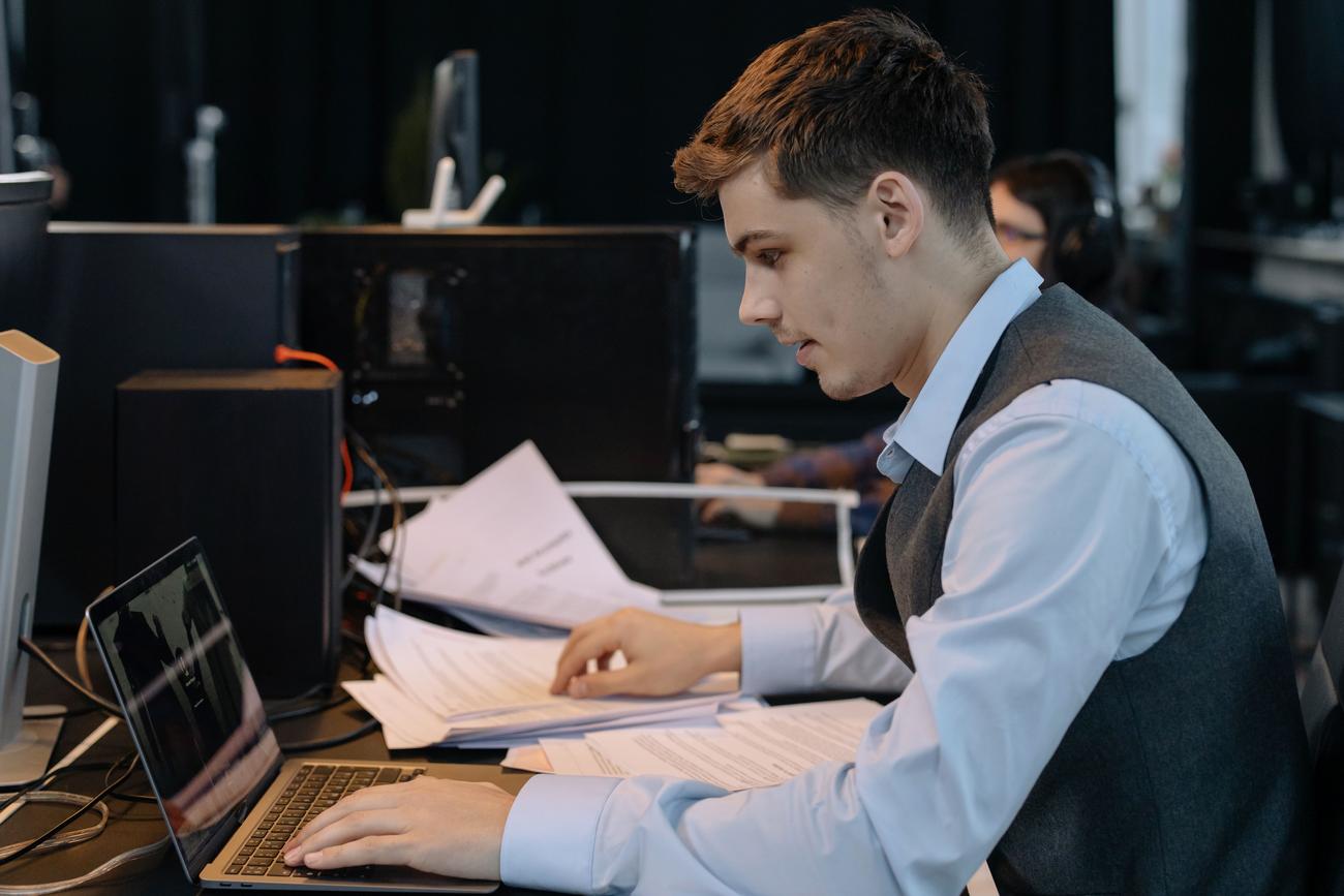 Profesional concentrado trabajando en una oficina moderna con un portátil y documentos, representando el trabajo profundo.