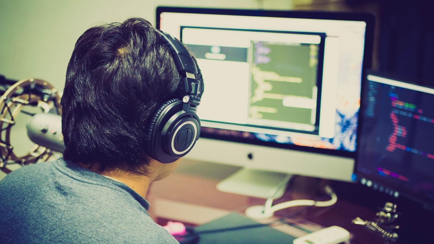 A programmer with headphones focuses on coding at a computer setup with dual monitors, illustrating the state of deep work and concentration.