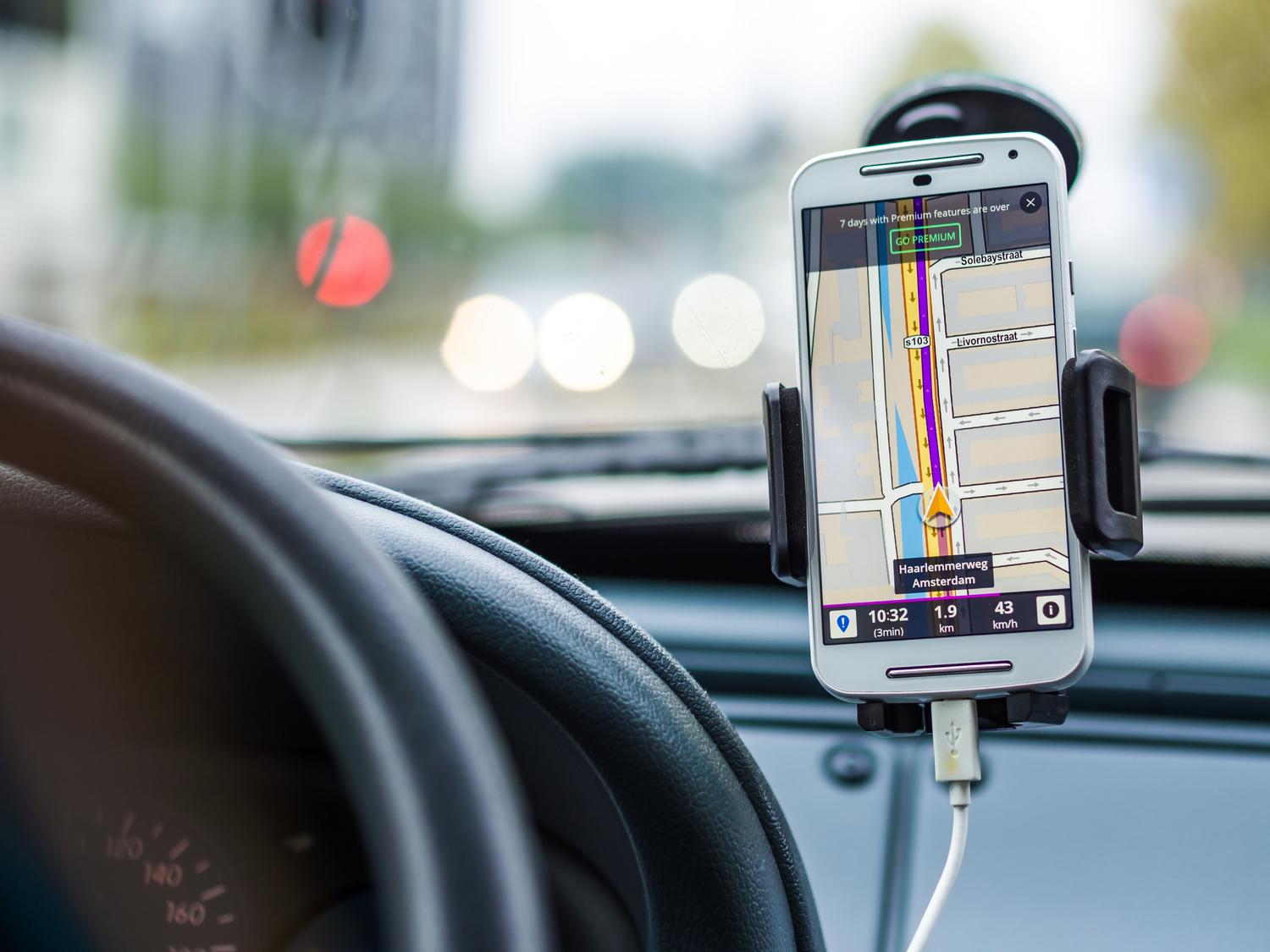 Smartphone montado en el salpicadero de un coche mostrando navegación GPS, ilustrando la conexión del móvil con el vehículo.