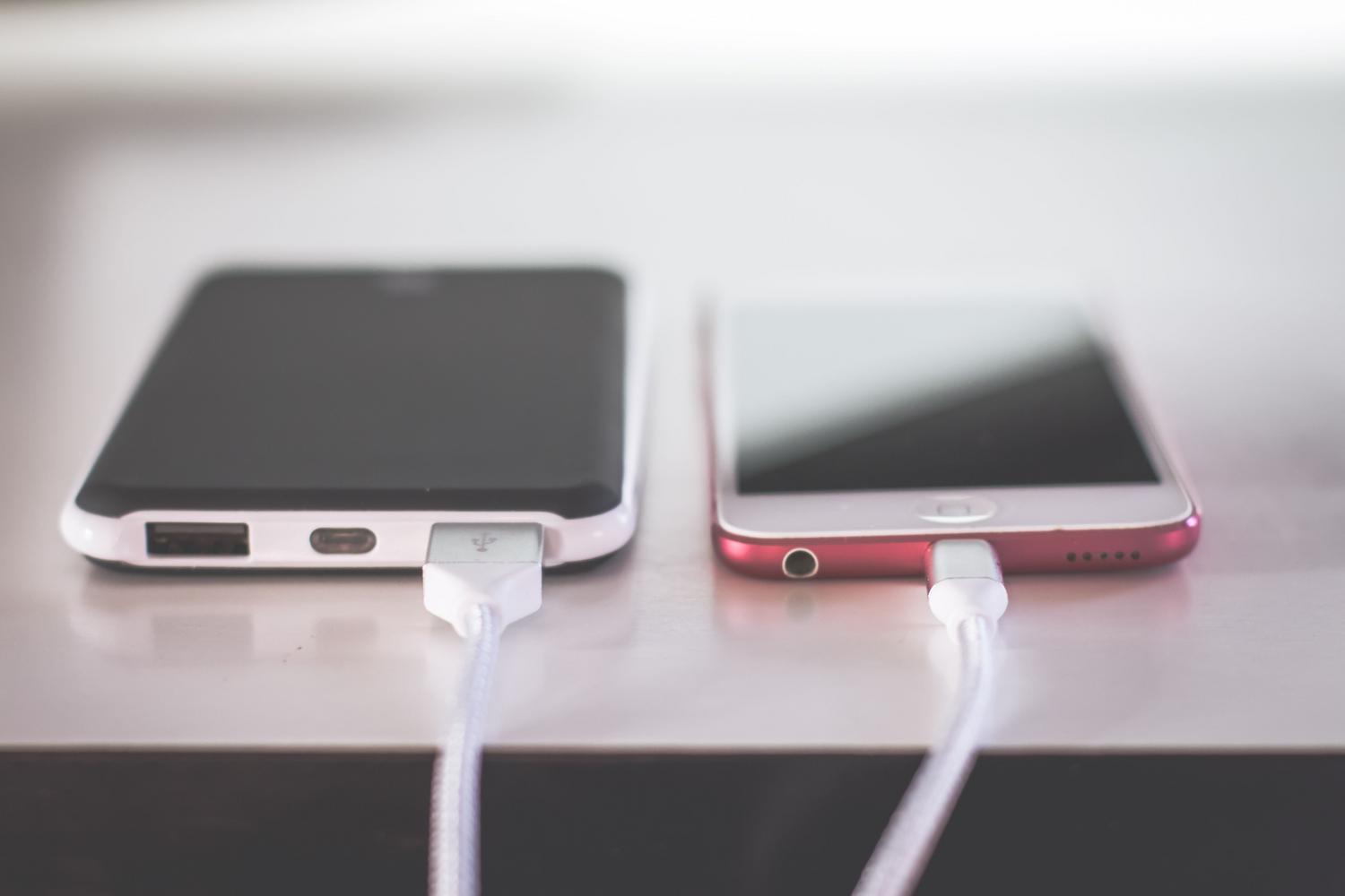 Dos smartphones conectados a sus cargadores lado a lado sobre una superficie blanca, ilustrando la importancia de mantener la energía durante la transferencia de datos.