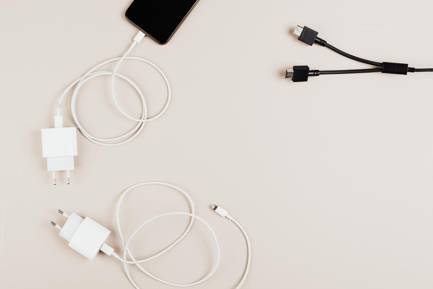Composición cenital de cables y adaptadores de carga sobre un fondo neutro, destacando los elementos esenciales para asegurar una alimentación eléctrica constante.