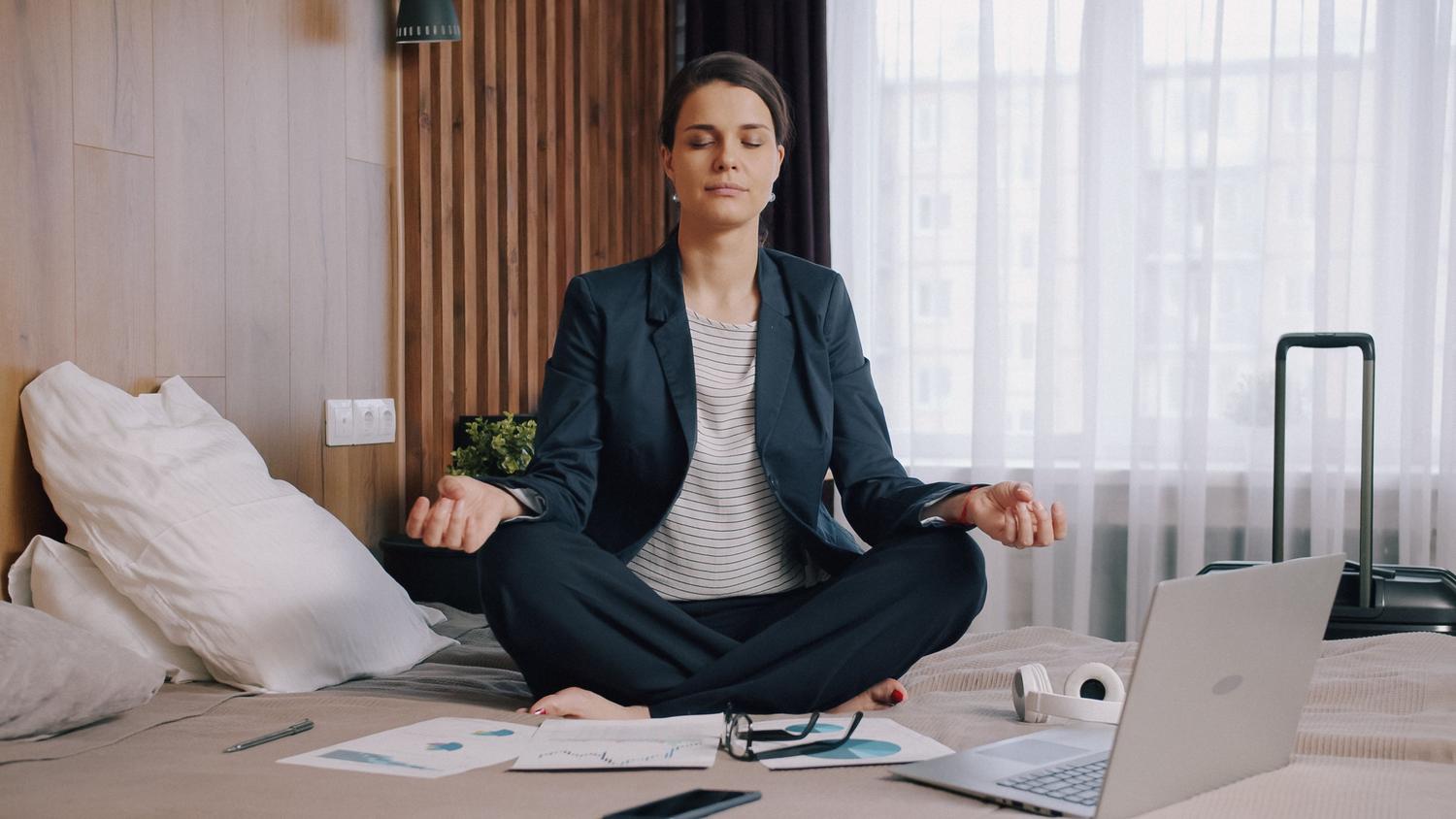 Mujer meditando en una habitación con herramientas de trabajo alrededor, representando el modo de descanso y la salud mental.