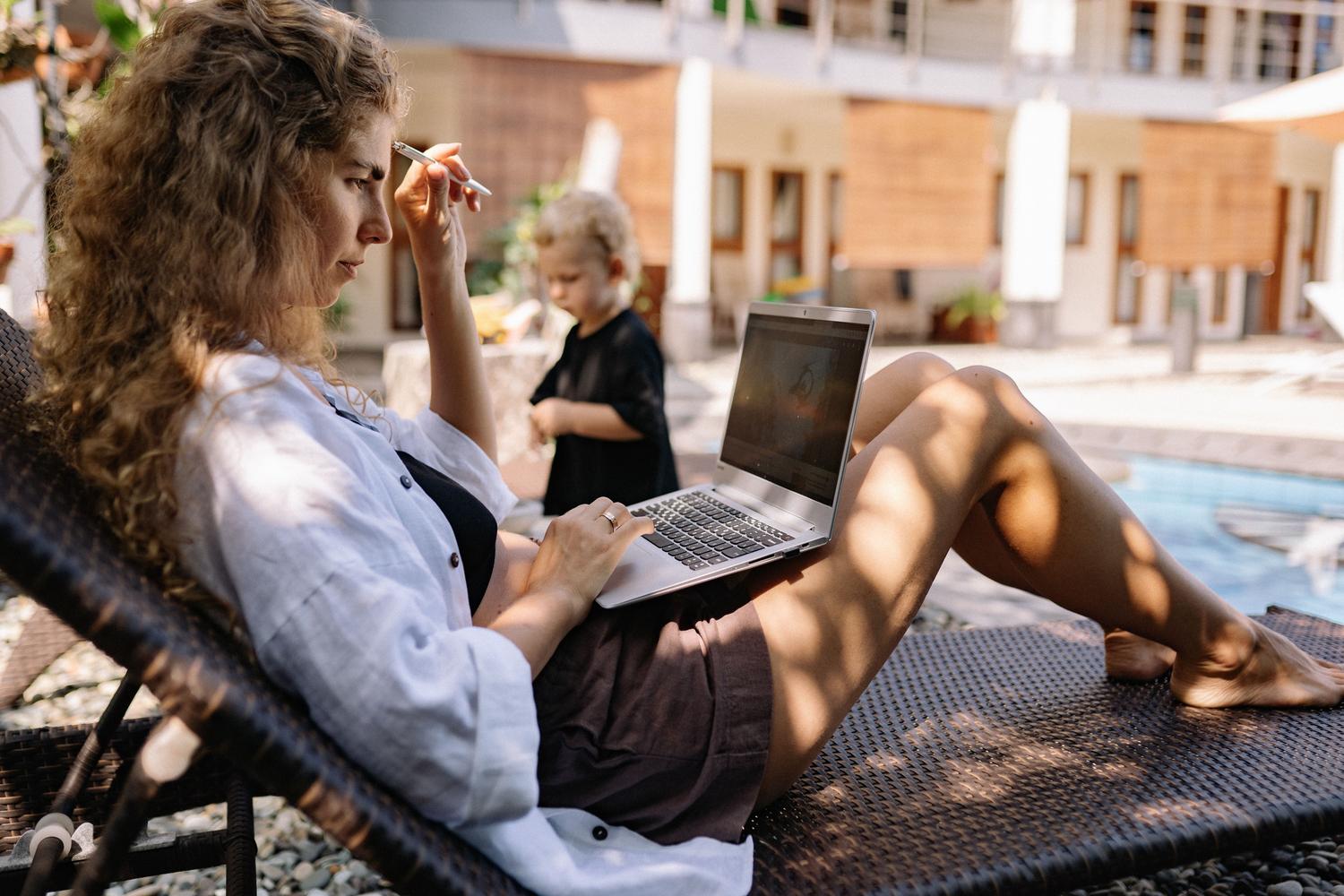 Mujer relajada usando un laptop junto a una piscina, mostrando la flexibilidad y el lado del ocio en la vida digital.