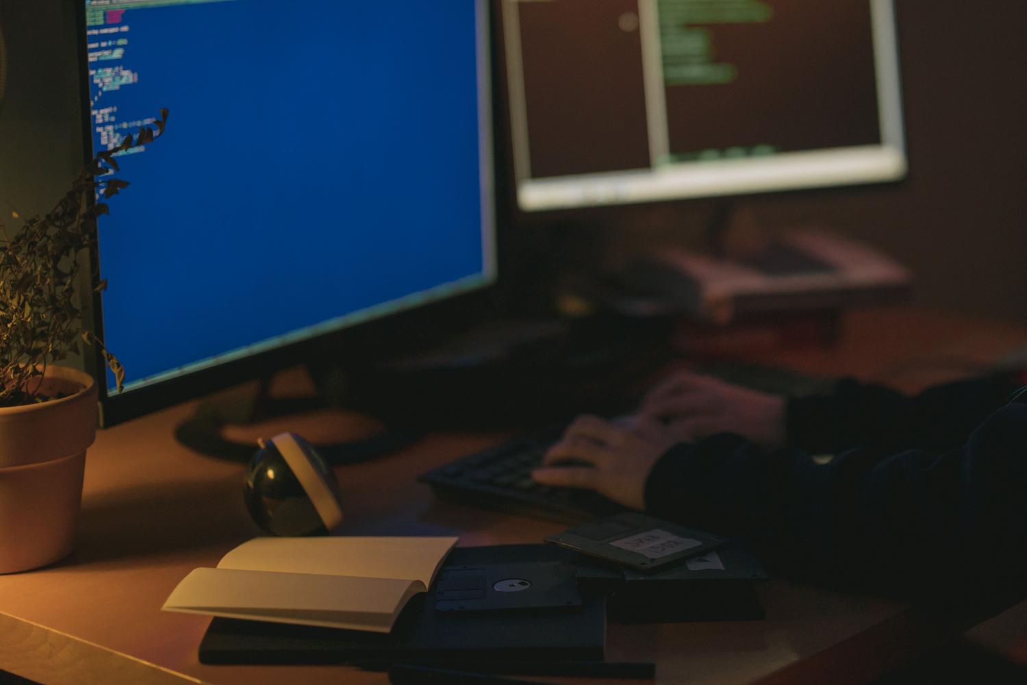 Programador trabajando en un entorno tenue con múltiples monitores para máxima productividad.