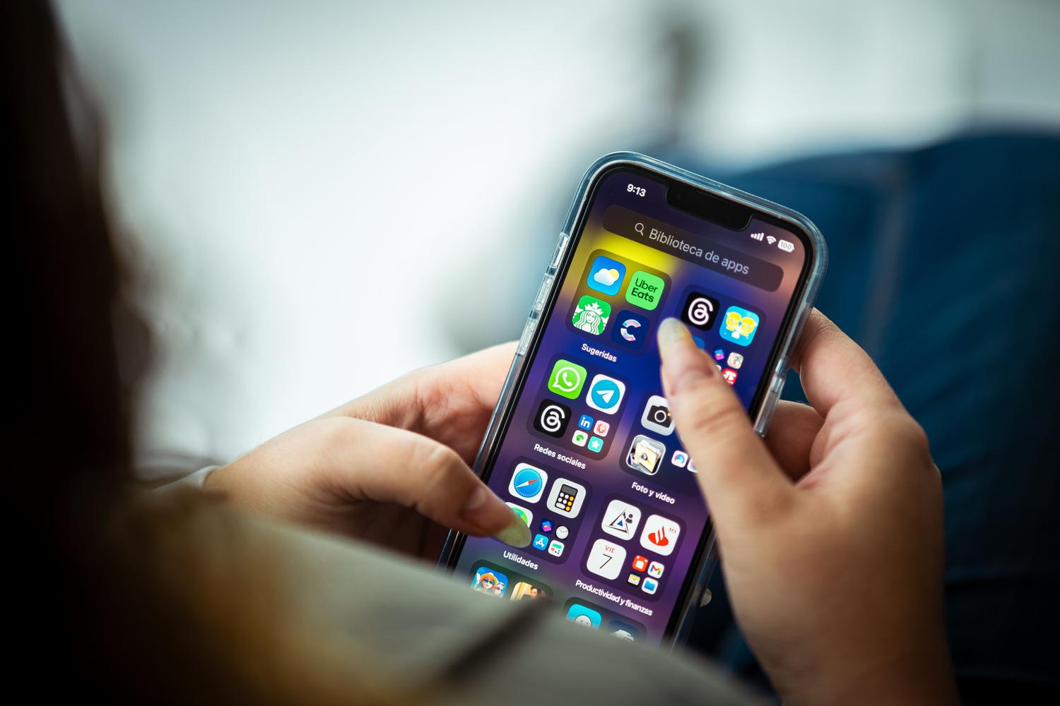 Primer plano de una persona sosteniendo un smartphone con diversas aplicaciones, ilustrando el entorno de iOS.