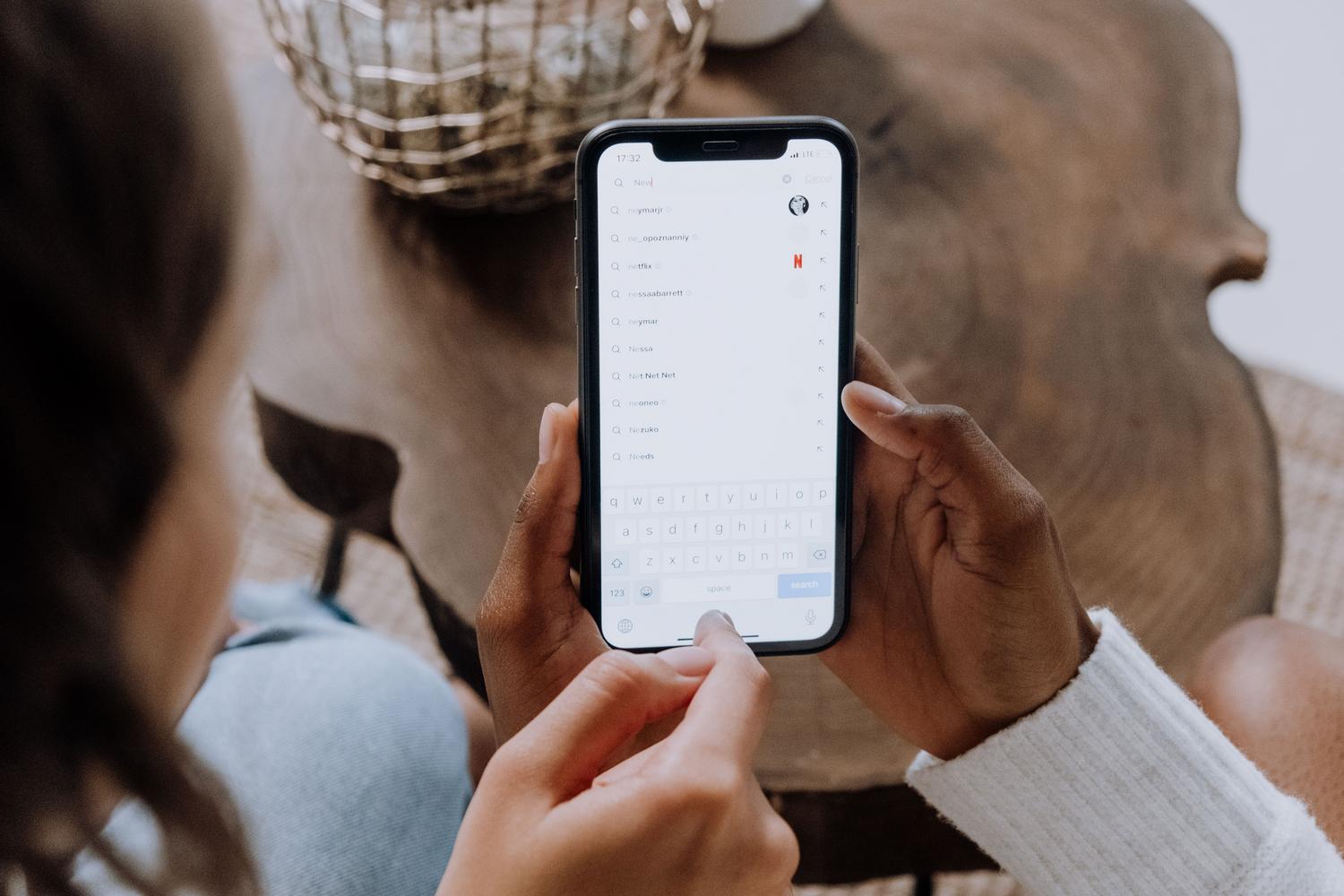 Manos buscando aplicaciones en un smartphone sobre una mesa de madera, representando el proceso de indexación y búsqueda en iOS.