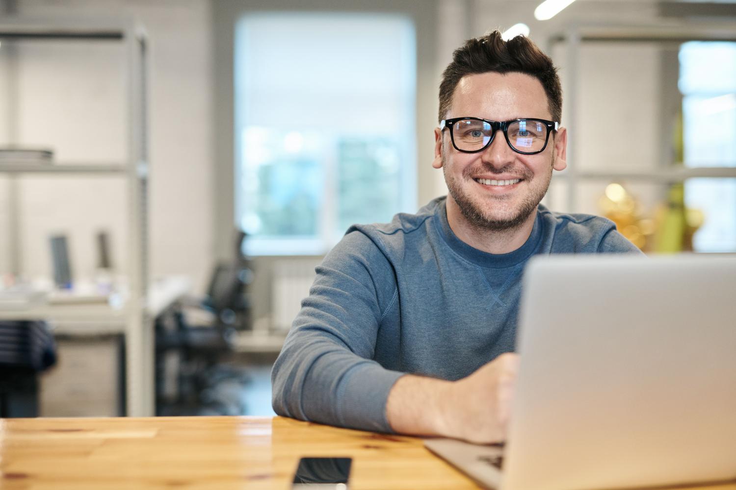 Hombre profesional sonriendo y relajado trabajando con su portátil, representando la productividad y el éxito.