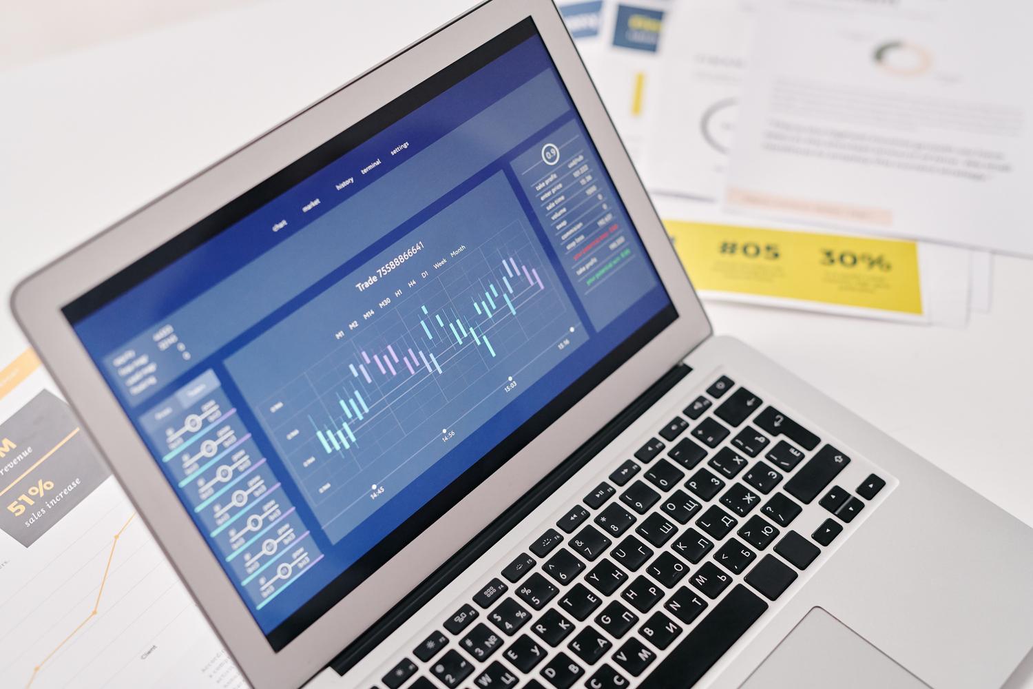 Espacio de trabajo profesional con un portátil y diversos informes de datos y gráficas impresas.