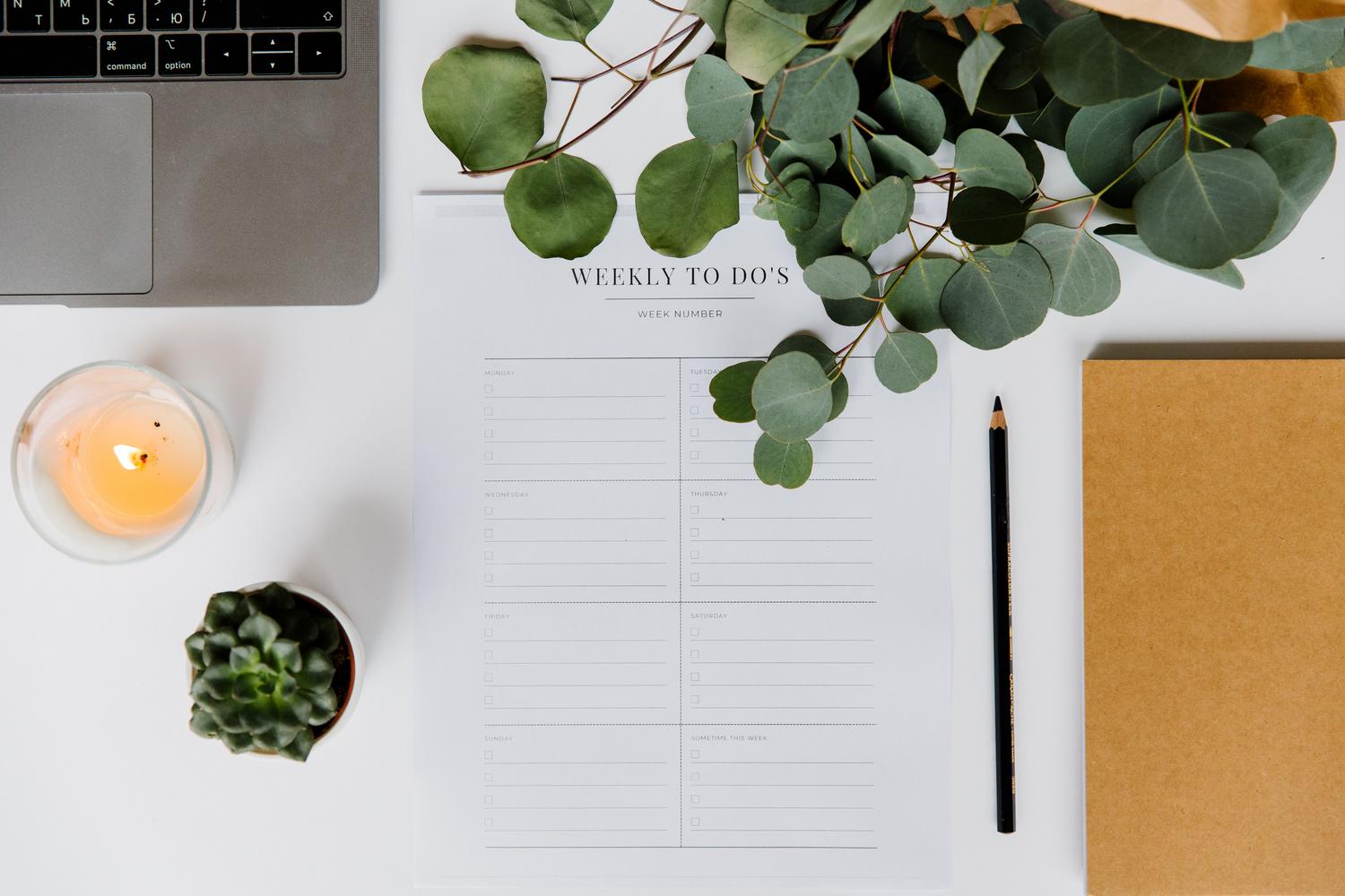 Espacio de trabajo minimalista y organizado con un portátil, una lista de tareas semanales y elementos naturales que transmiten calma y enfoque.