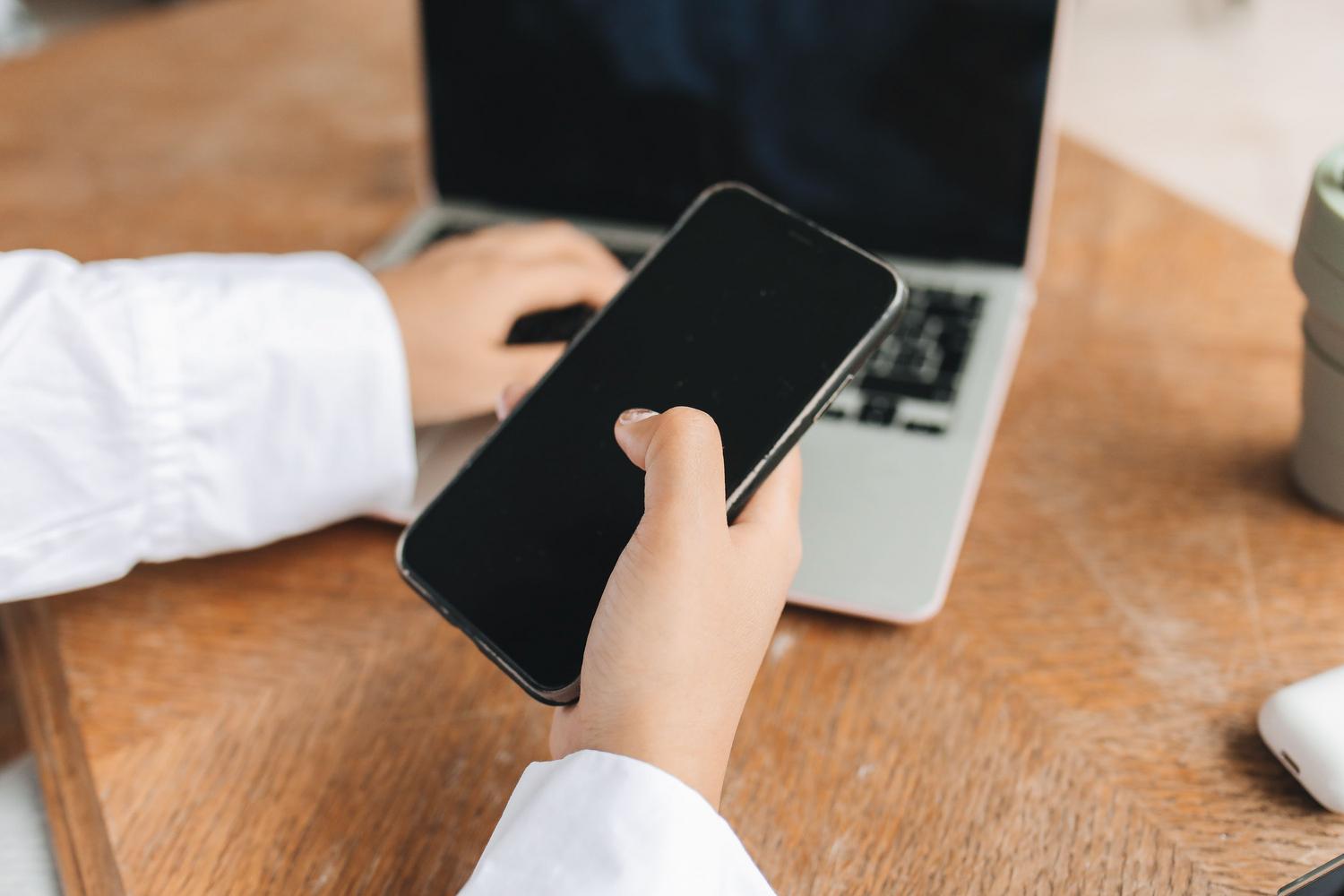 Persona organizando su trabajo remoto con un smartphone y un portátil en un escritorio doméstico, representando el equilibrio entre vida laboral y personal.