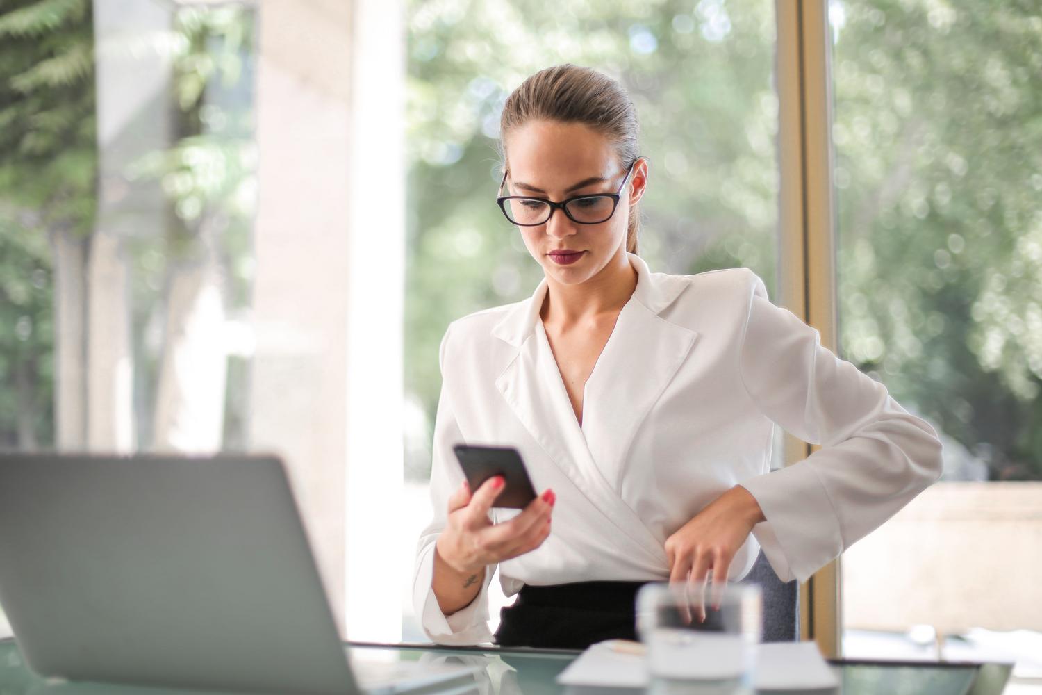 Mujer ejecutiva manejando su smartphone en su puesto de trabajo, enfocada en la productividad.