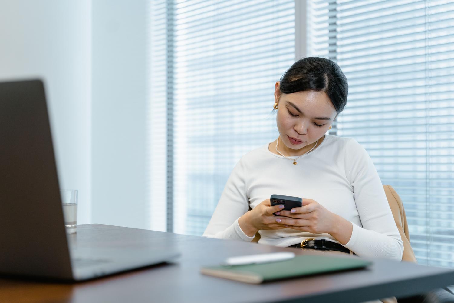Mujer profesional utilizando el teléfono móvil en un entorno de oficina moderno y luminoso.