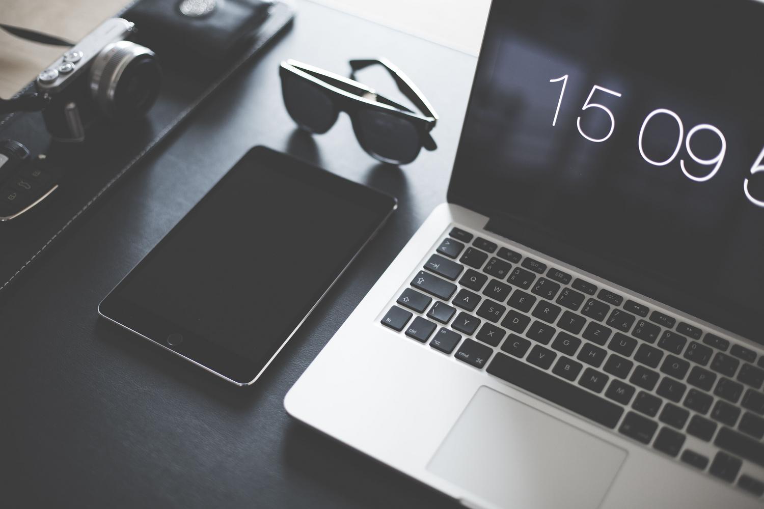 Espacio de trabajo minimalista con MacBook y iPad sobre una superficie oscura, ideal para un entorno de productividad profesional.