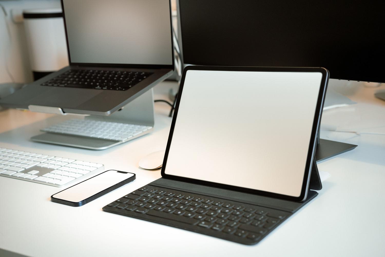 Configuración de oficina moderna con laptop en soporte y tablet con teclado, mostrando un ecosistema de dispositivos interconectados.
