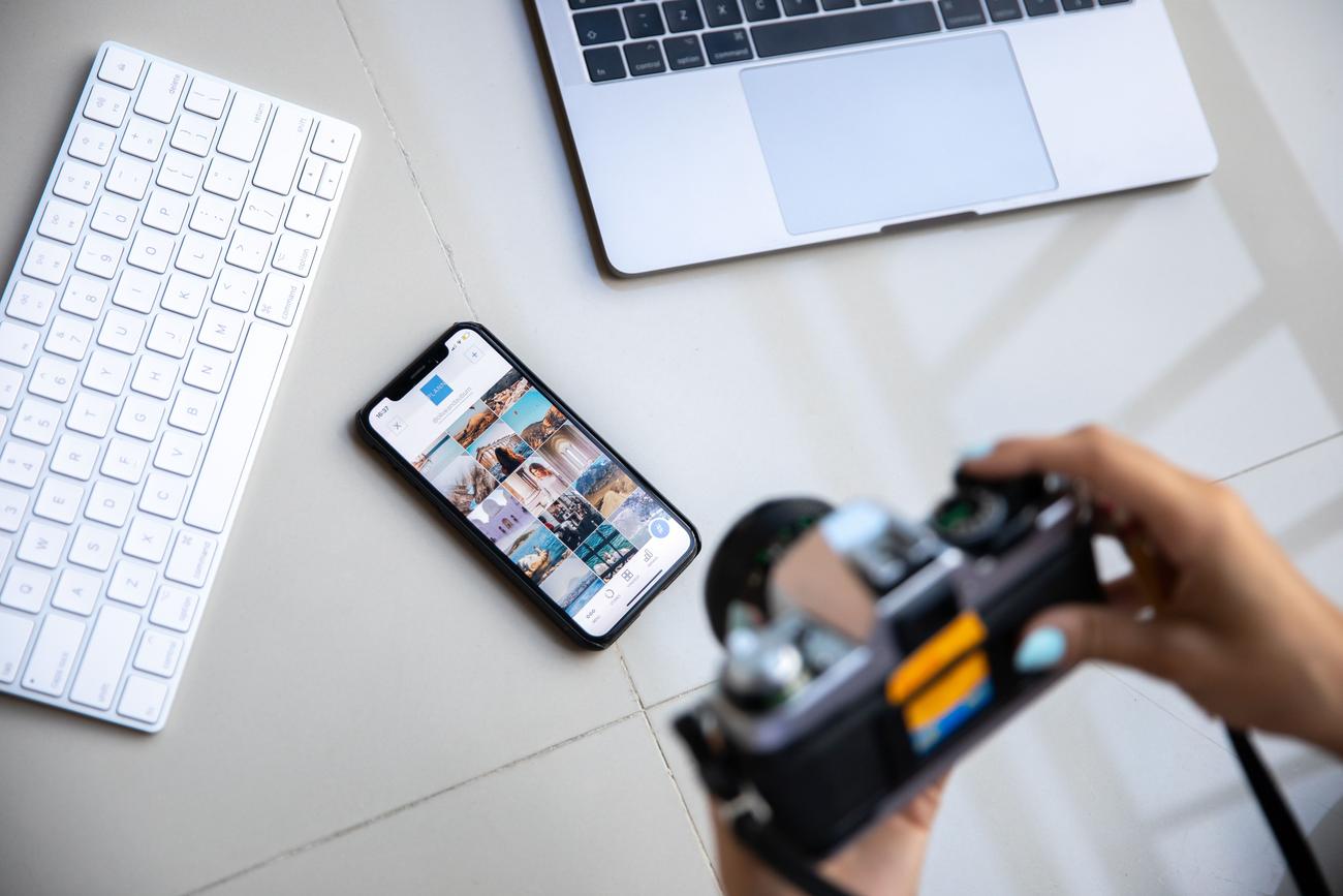 Espacio de trabajo moderno de un fotógrafo que combina una cámara vintage, un smartphone y un ordenador portátil.
