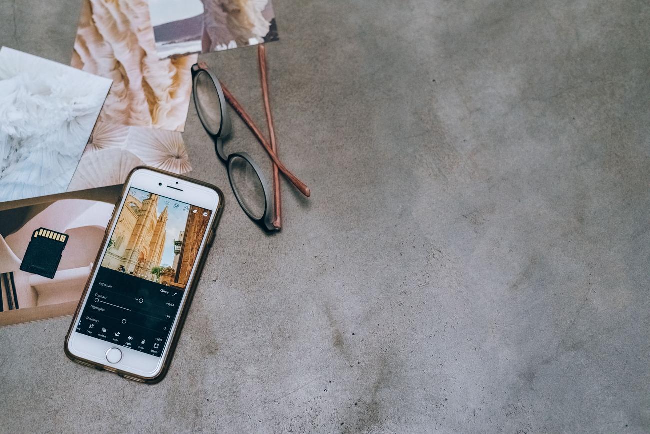 Smartphone y gafas sobre una superficie de hormigón con fotografías impresas y una tarjeta de memoria, representando el ecosistema de la fotografía móvil.