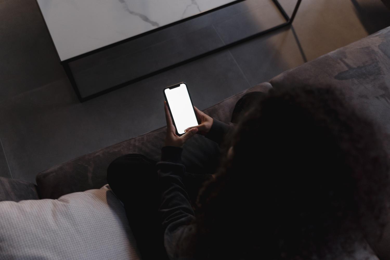 Persona sosteniendo un smartphone mientras descansa en un sofá, simbolizando la tranquilidad de tener espacio suficiente en el dispositivo.
