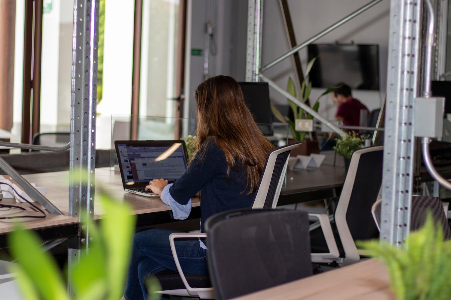 Mujer trabajando concentrada con su ordenador portátil en un espacio de coworking moderno y luminoso, representando la productividad personal.