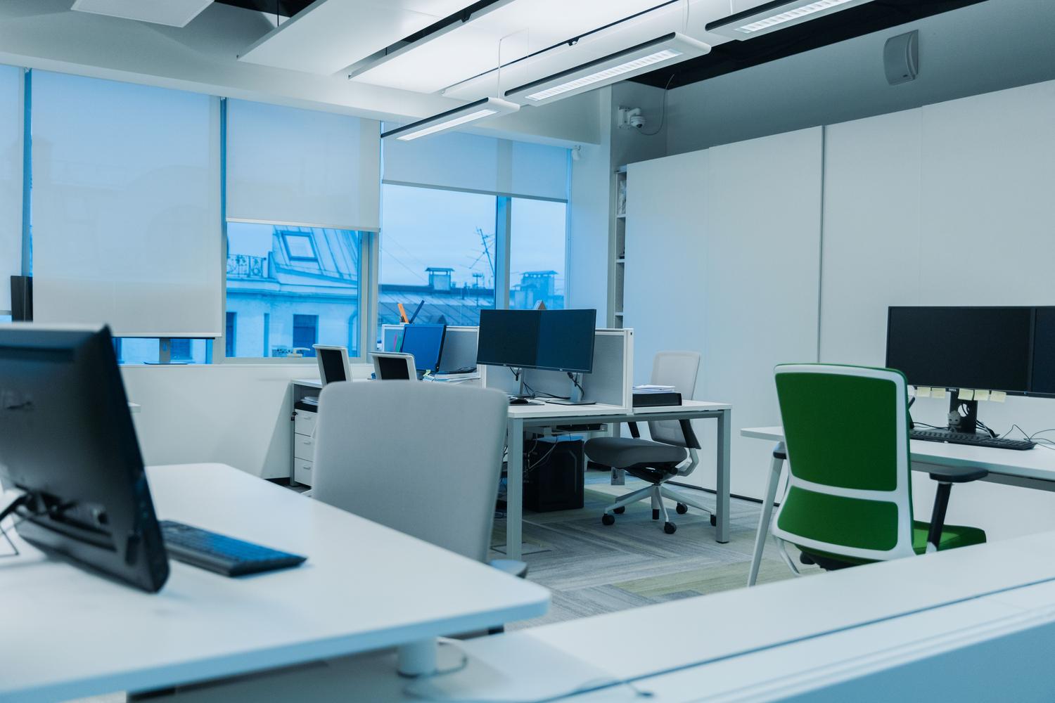 Entorno de oficina moderno, amplio y luminoso con estaciones de trabajo, que evoca un ambiente profesional y organizado.