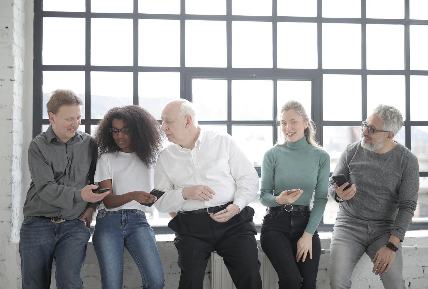 Grupo multicultural de colegas compartiendo un smartphone, simbolizando el modo conversación y la comunicación global.