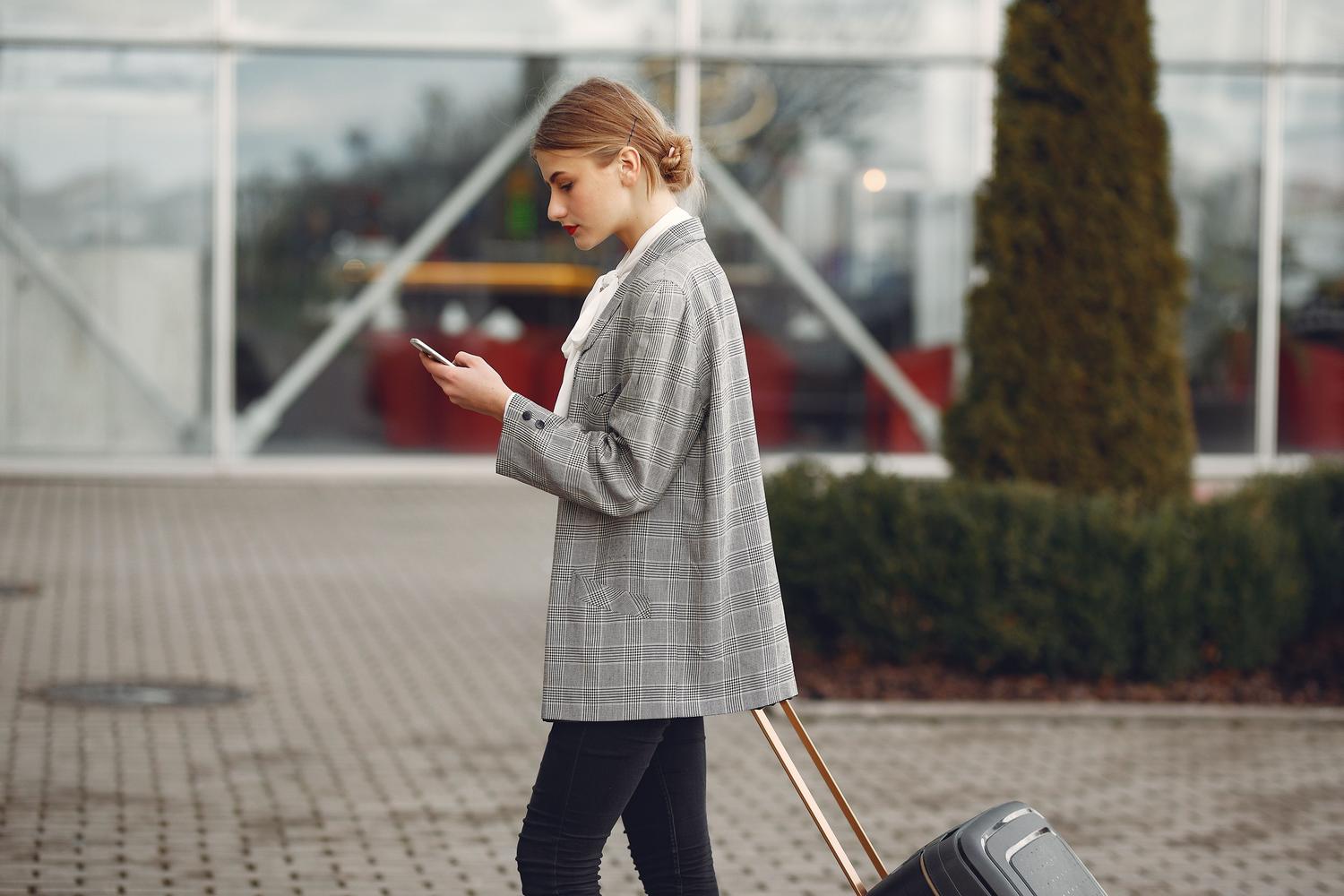 Mujer viajera utilizando su smartphone mientras camina con una maleta, representando la traducción instantánea en viajes.