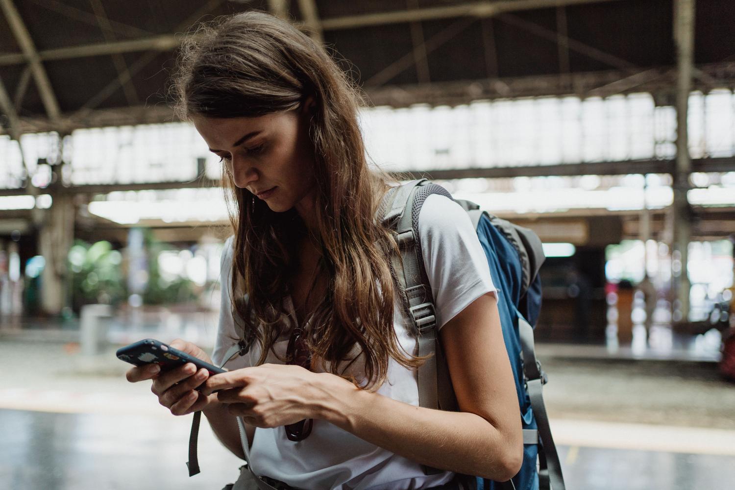 Mujer joven consultando su teléfono móvil en una estación de tren, ilustrando el uso de Google Translate en situaciones cotidianas de viaje.