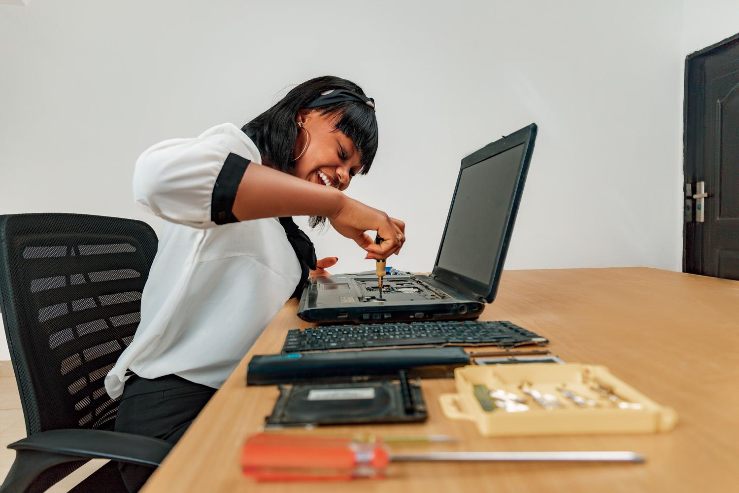 Una mujer realizando el mantenimiento técnico de un ordenador portátil en un escritorio con herramientas especializadas.