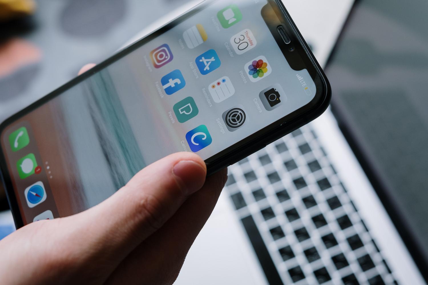 Persona utilizando un smartphone frente a un ordenador portátil, destacando la conectividad del ecosistema digital.