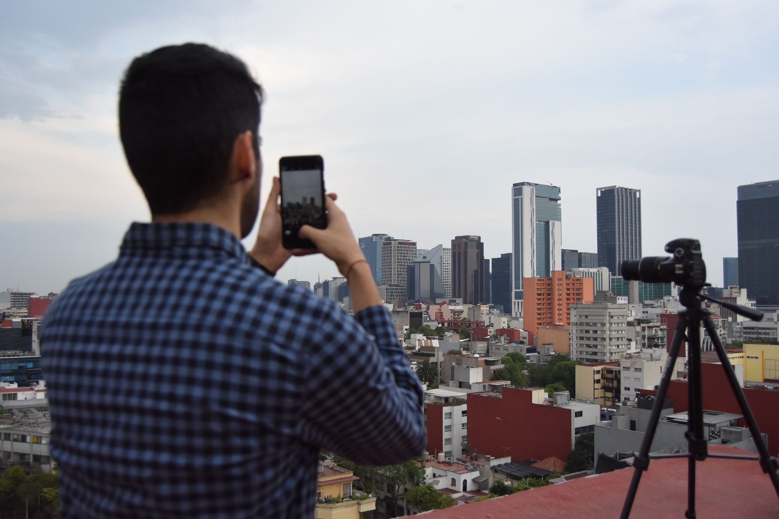 Fotógrafo capturando la panorámica de una ciudad desde una azotea con un smartphone, representando la fotografía de paisaje en modo profesional.