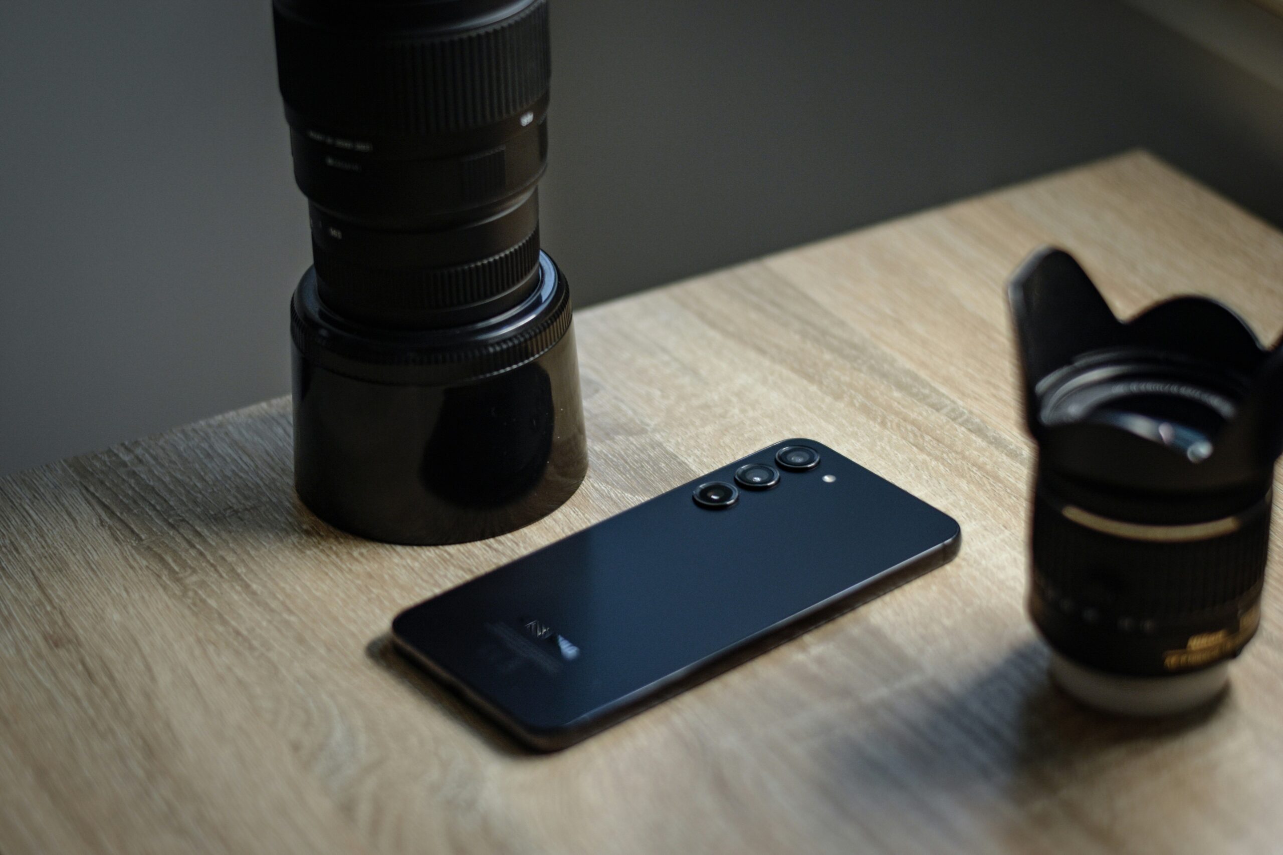 Un smartphone moderno junto a lentes de cámara profesionales sobre un escritorio de madera, simbolizando la calidad profesional de la fotografía móvil.