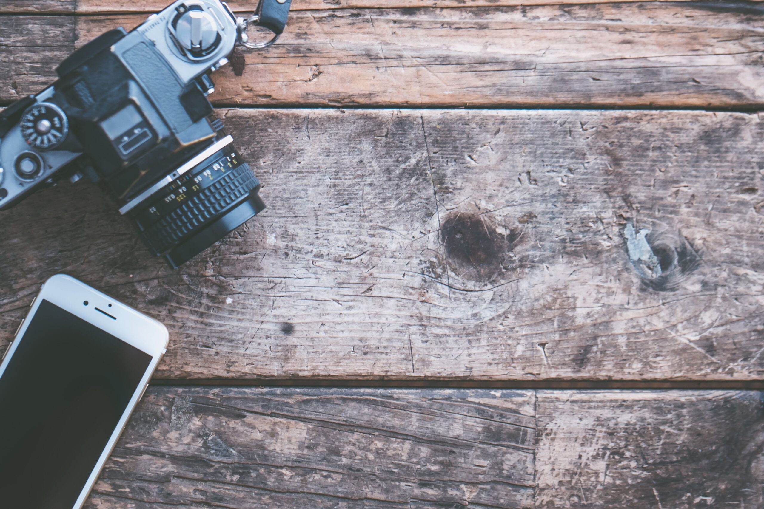 Comparativa visual entre una cámara réflex vintage y un smartphone moderno sobre una superficie rústica, representando la evolución hacia la fotografía digital móvil.