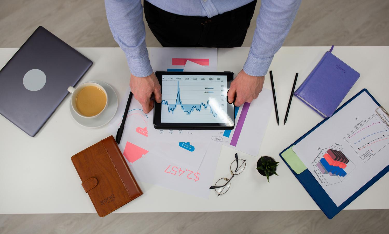 Persona utilizando una tablet para revisar gráficos sobre documentos impresos, destacando la versatilidad de los dispositivos móviles y la sincronización.