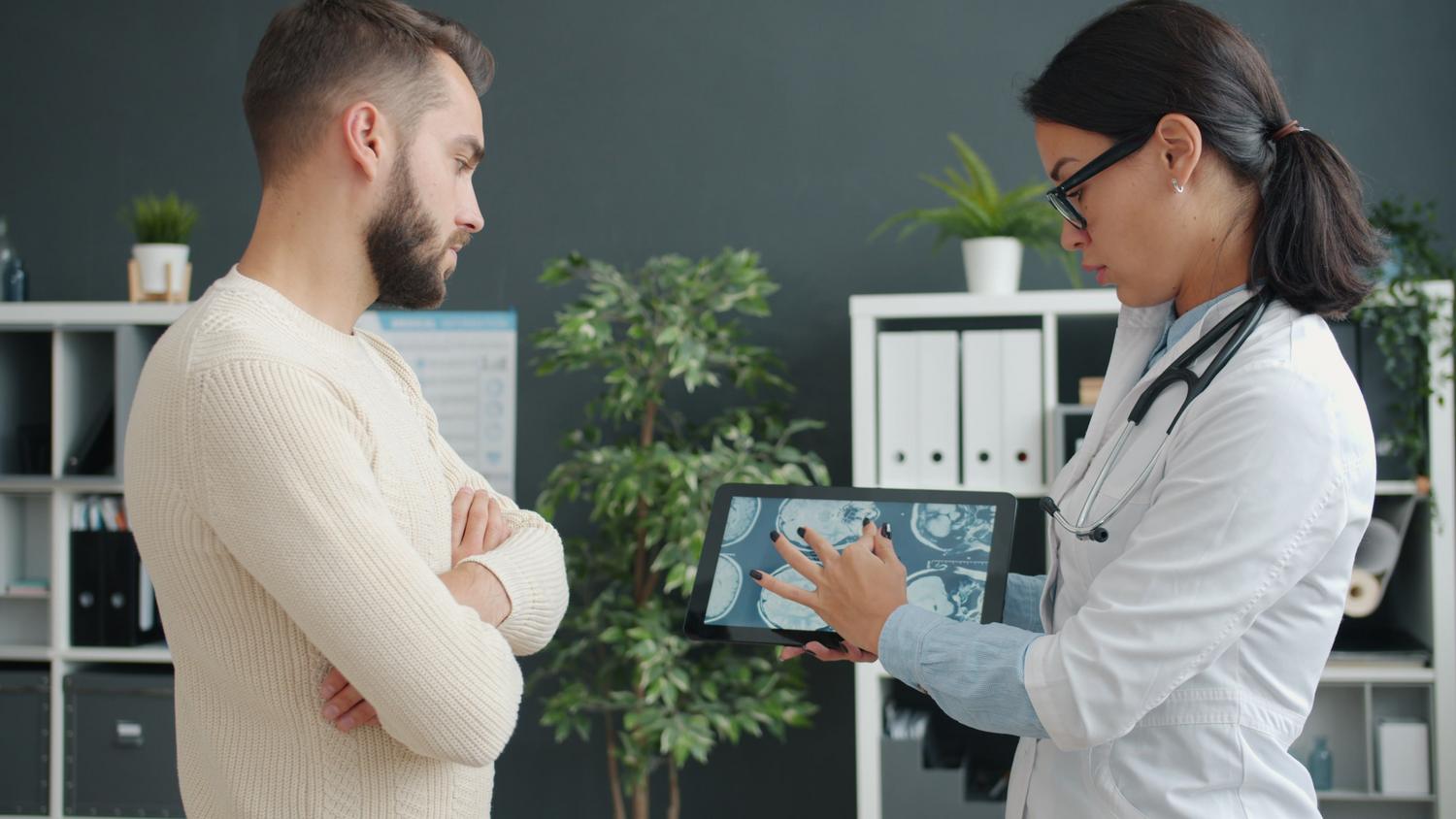 Médico mostrando resultados de una resonancia magnética digital en una tableta a su paciente.