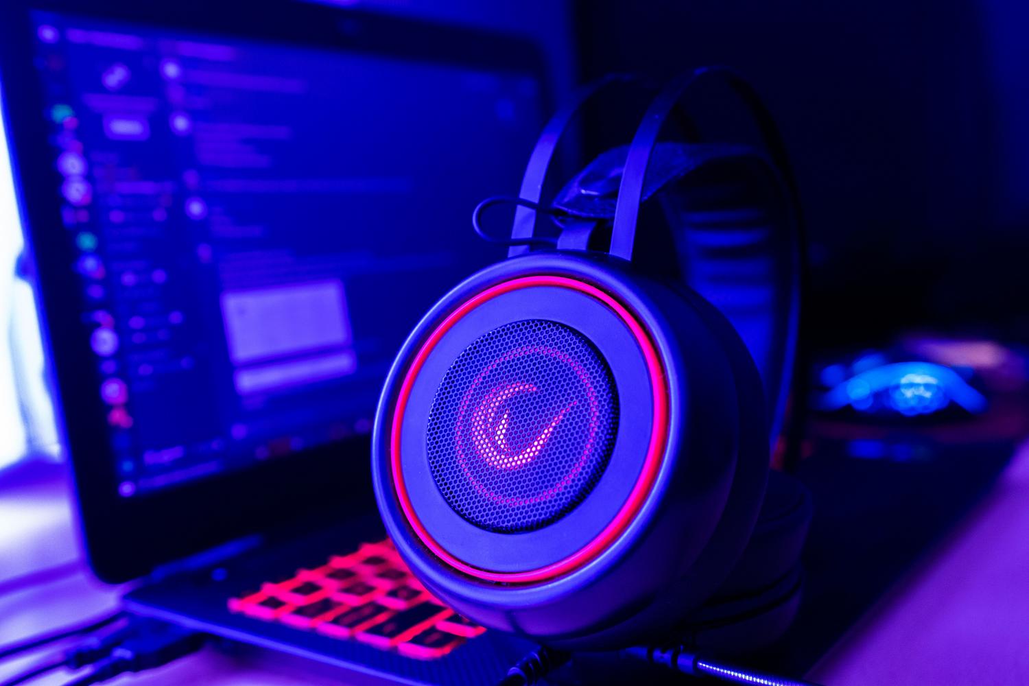 Primer plano de auriculares gaming y un portátil con iluminación neón, simbolizando la tecnología necesaria para el chat de proximidad y el juego cruzado.