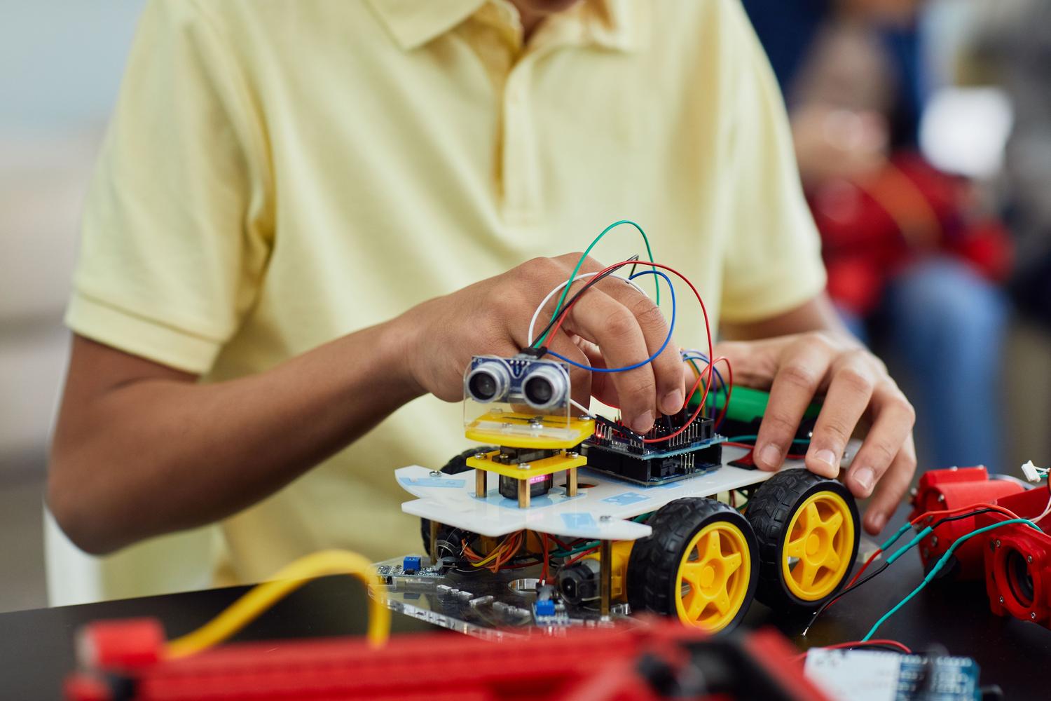 Estudiante de primaria ensamblando un coche robot con cables y sensores, representando el aprendizaje práctico STEM.