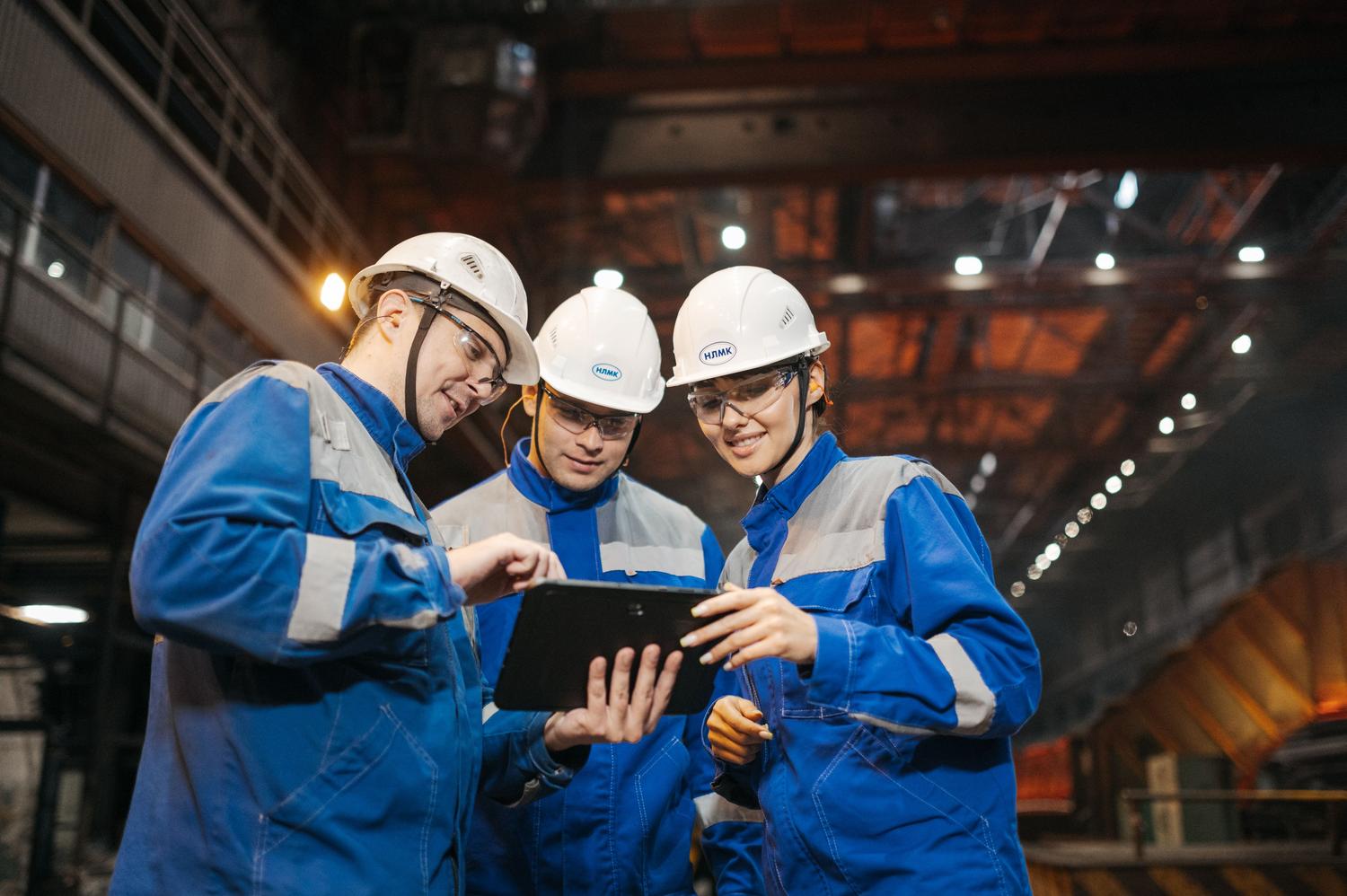 Ingenieros industriales colaborando y analizando datos en una tablet dentro de una fábrica inteligente.