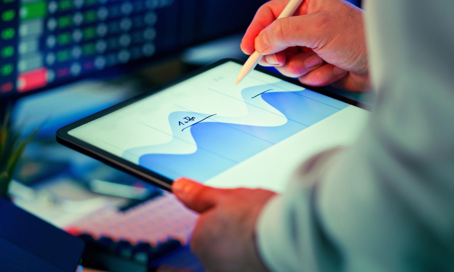Profesional analizando gráficos de datos en una tablet en un entorno de oficina moderno, representando la movilidad y el acceso a datos.