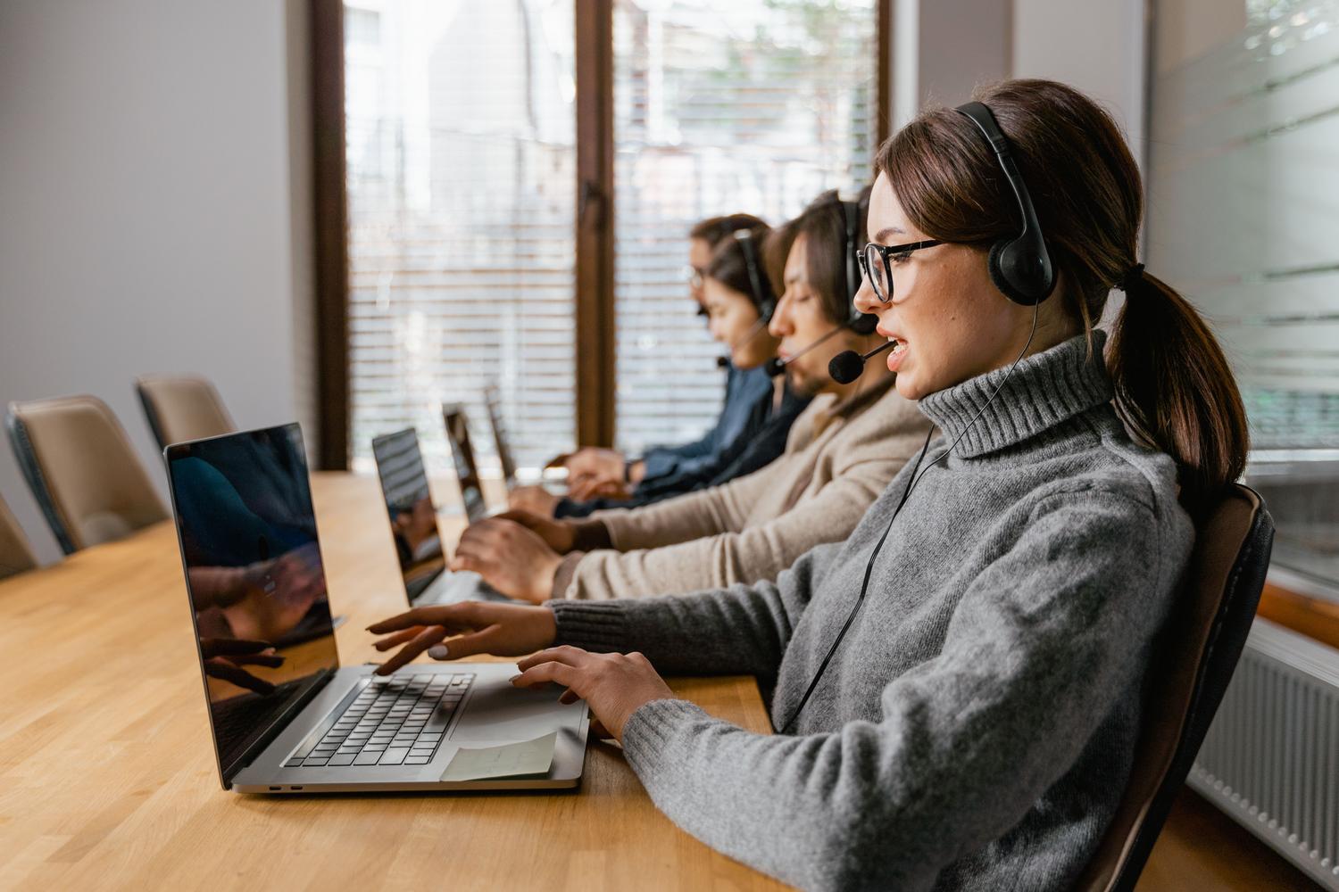 Equipo de atención al cliente trabajando con laptops y auriculares en un espacio de oficina contemporáneo.