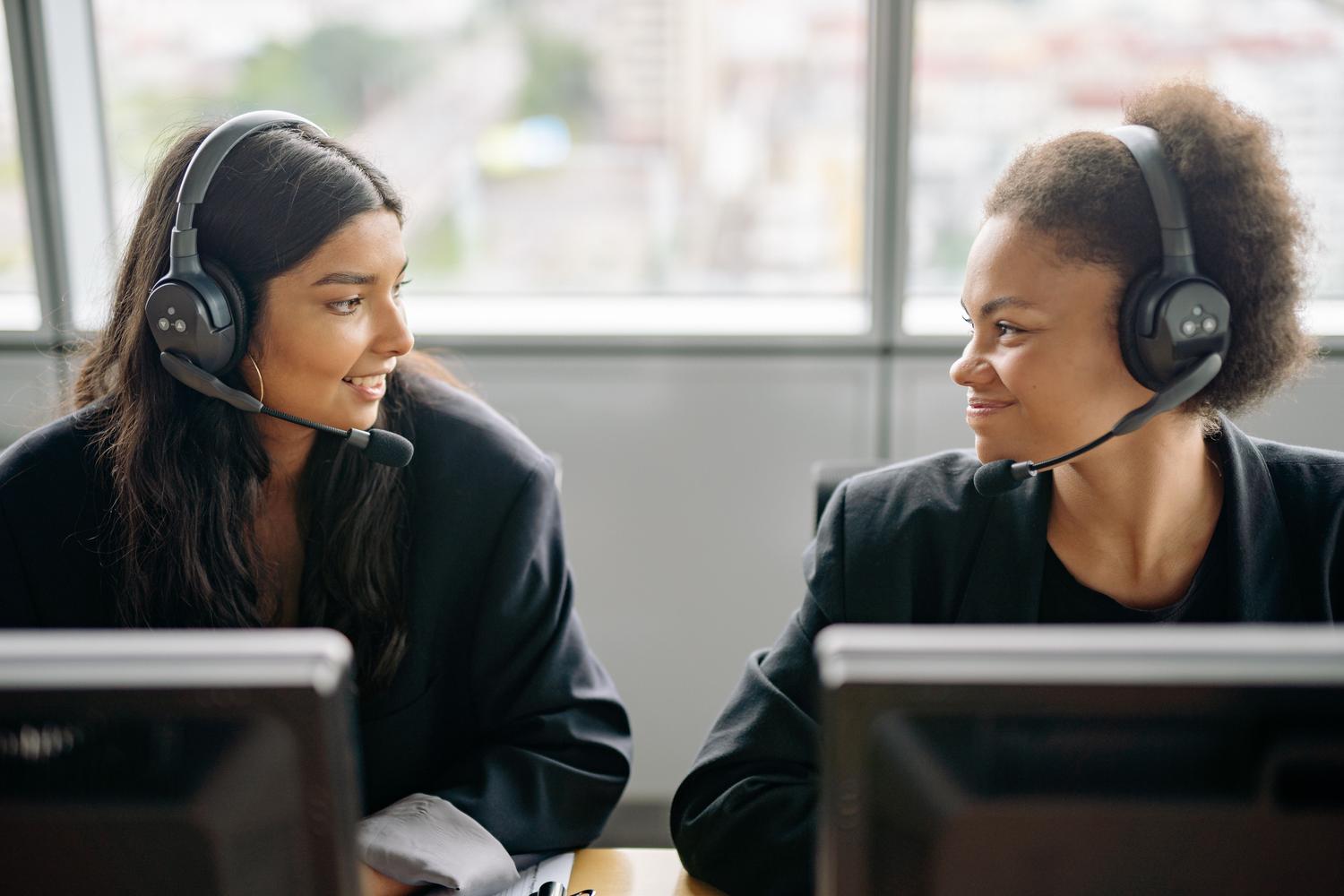 Dos profesionales de soporte al cliente colaborando y sonriendo en un entorno empresarial moderno.