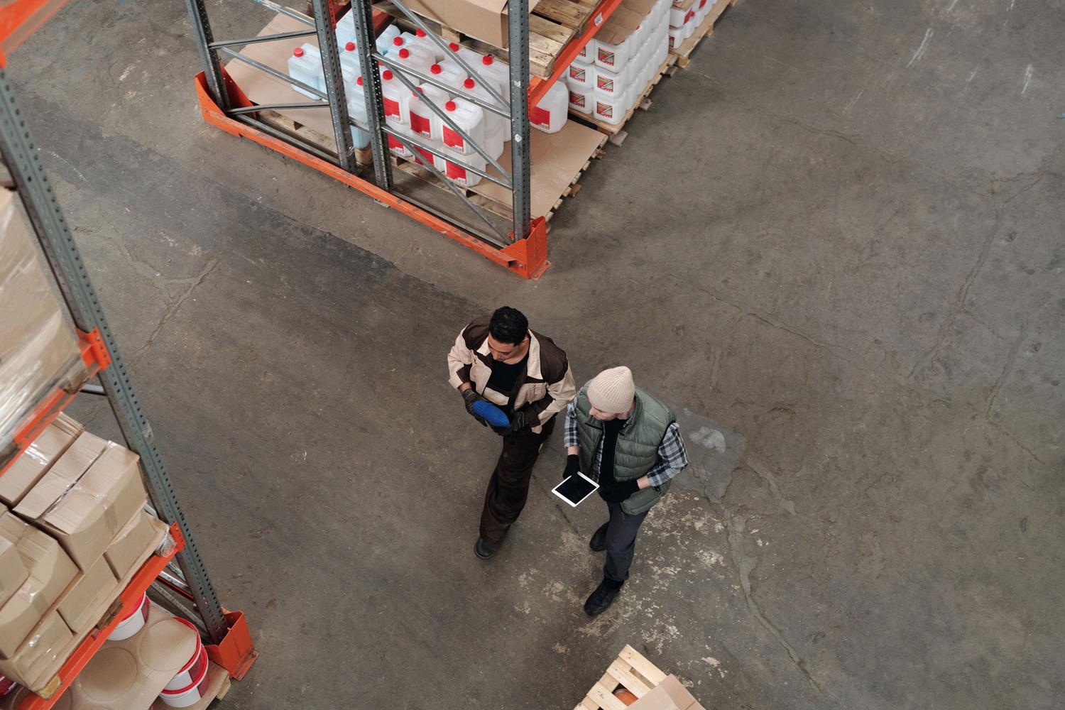Dos profesionales de logística coordinando el stock mediante una tablet en un almacén, simbolizando la sincronización de datos y la colaboración departamental.