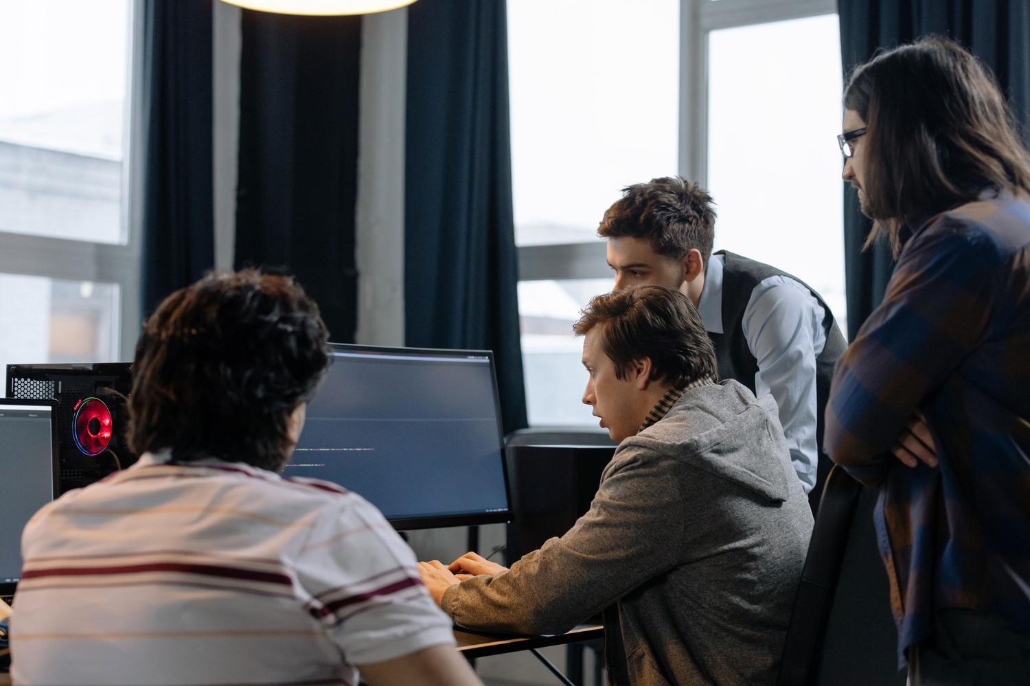 Equipo de desarrolladores de software colaborando en la revisión de código frente a un monitor en una oficina moderna.