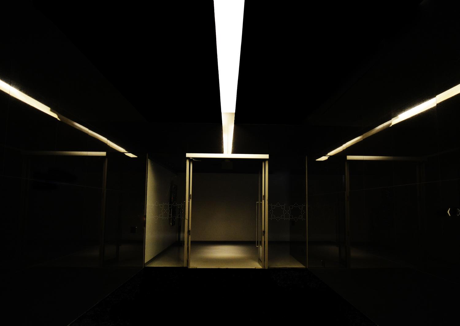 Pasillo subterráneo minimalista y frío que representa el silencio opresivo y la arquitectura hostil del complejo.