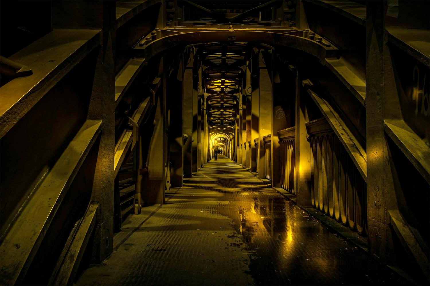 Túnel de acero con luces ámbar y suelos húmedos que encapsulan la estética del horror industrial.