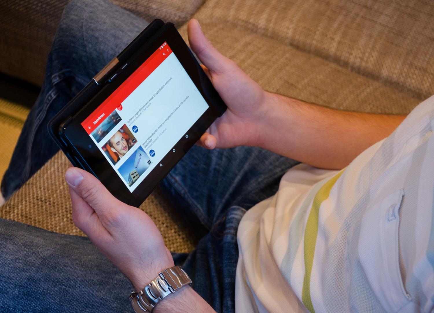Persona consumiendo contenido multimedia y noticias en una tablet desde un sofá, ilustrando la capacidad de streaming y vídeo.
