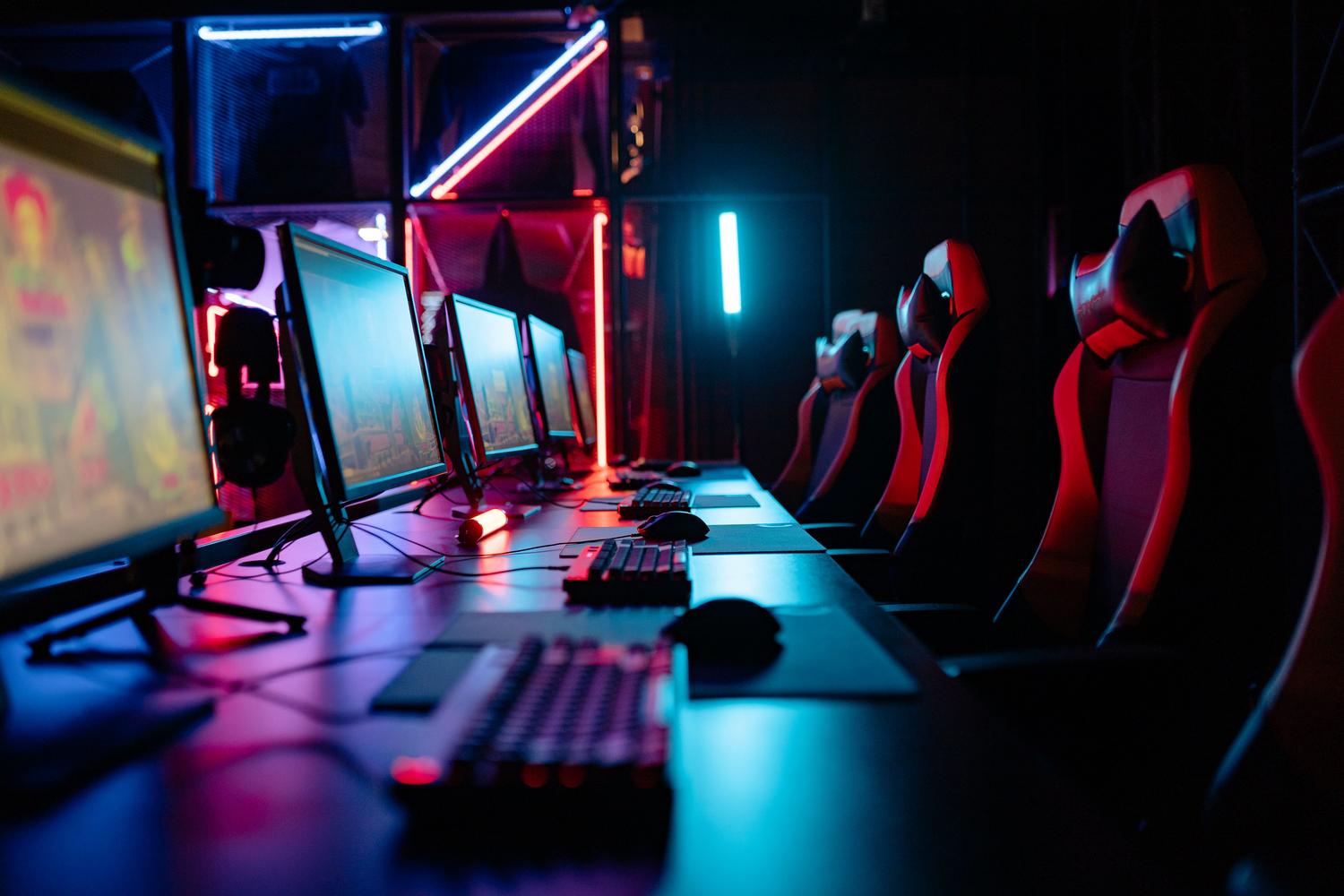 Habitación de gaming inmersiva con luces de neón y múltiples estaciones de juego, evocando la atmósfera del mundo del gaming competitivo.