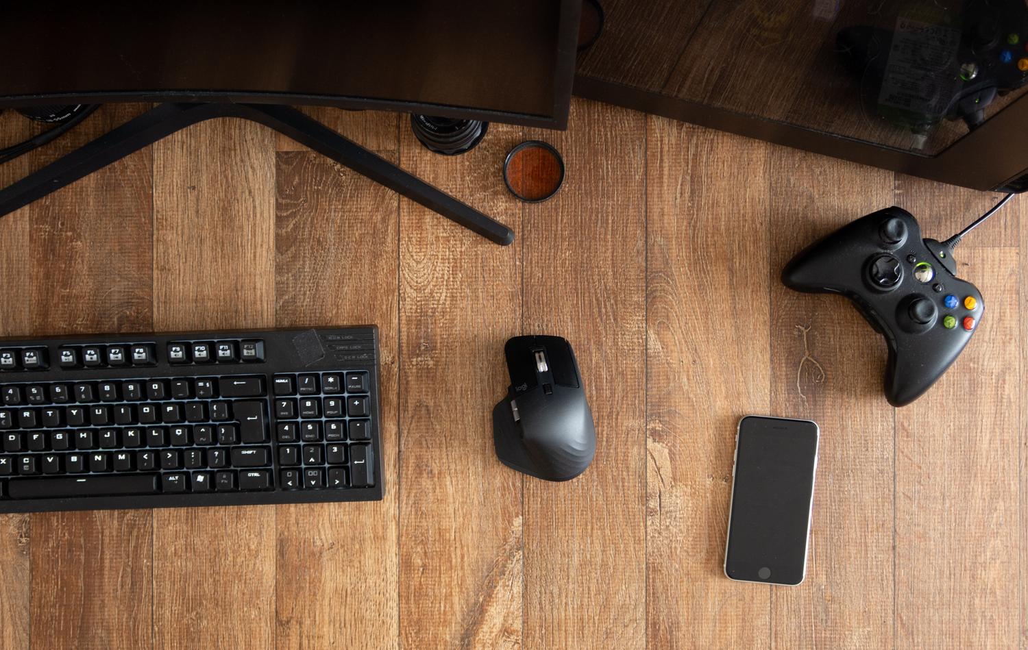 Vista cenital de un gamepad, teclado y ratón sobre una mesa de madera.