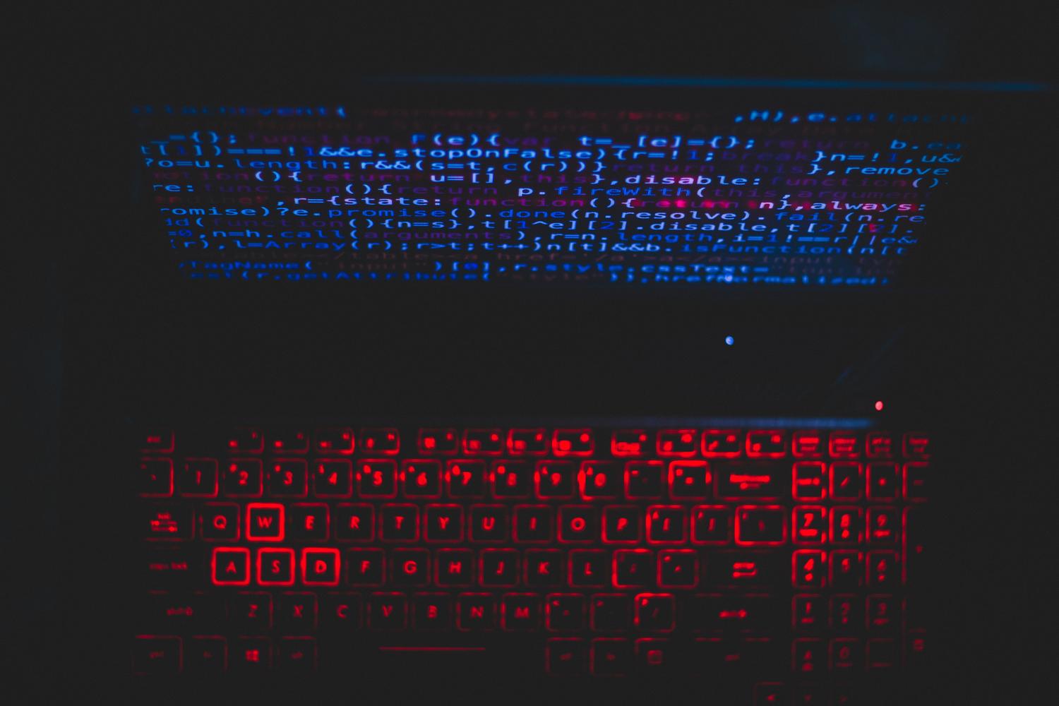 Pantalla con código de programación y teclado retroiluminado en rojo, simbolizando el análisis y parcheo de vulnerabilidades.