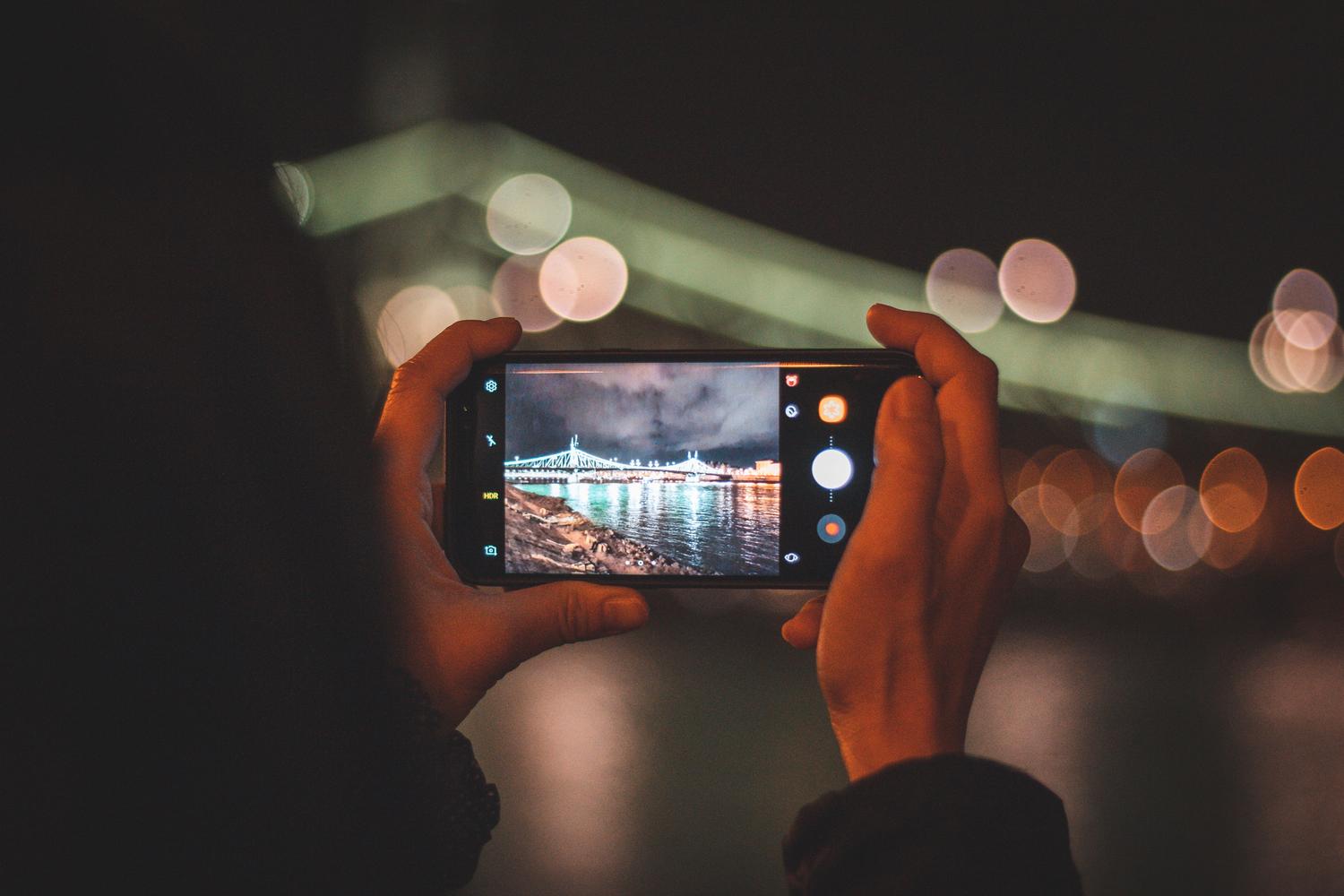 Persona capturando el paisaje urbano de una ciudad por la noche con un smartphone