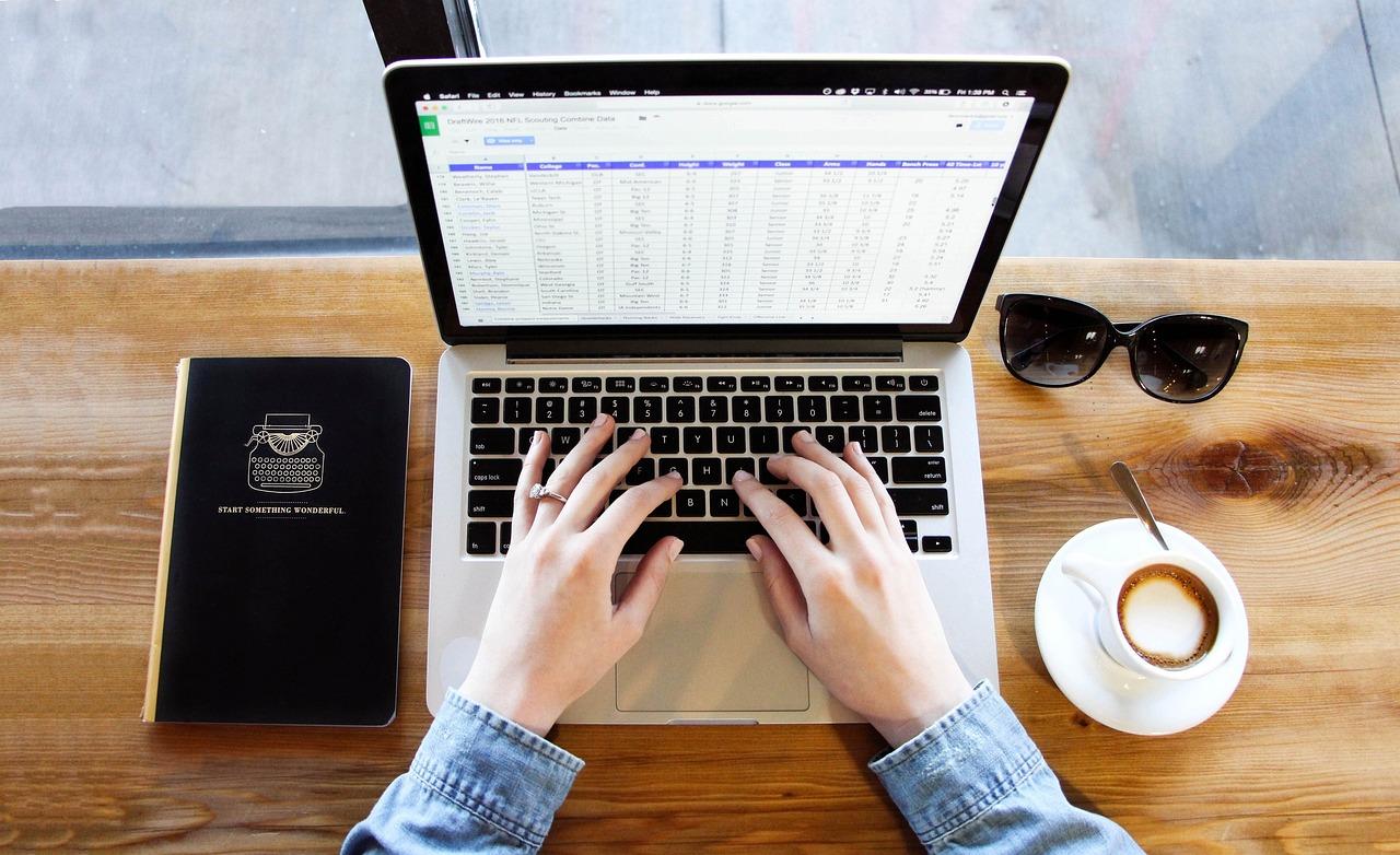 Persona trabajando en un ordenador portátil con un café, ilustrando la productividad y el uso de atajos de teclado en hojas de cálculo.