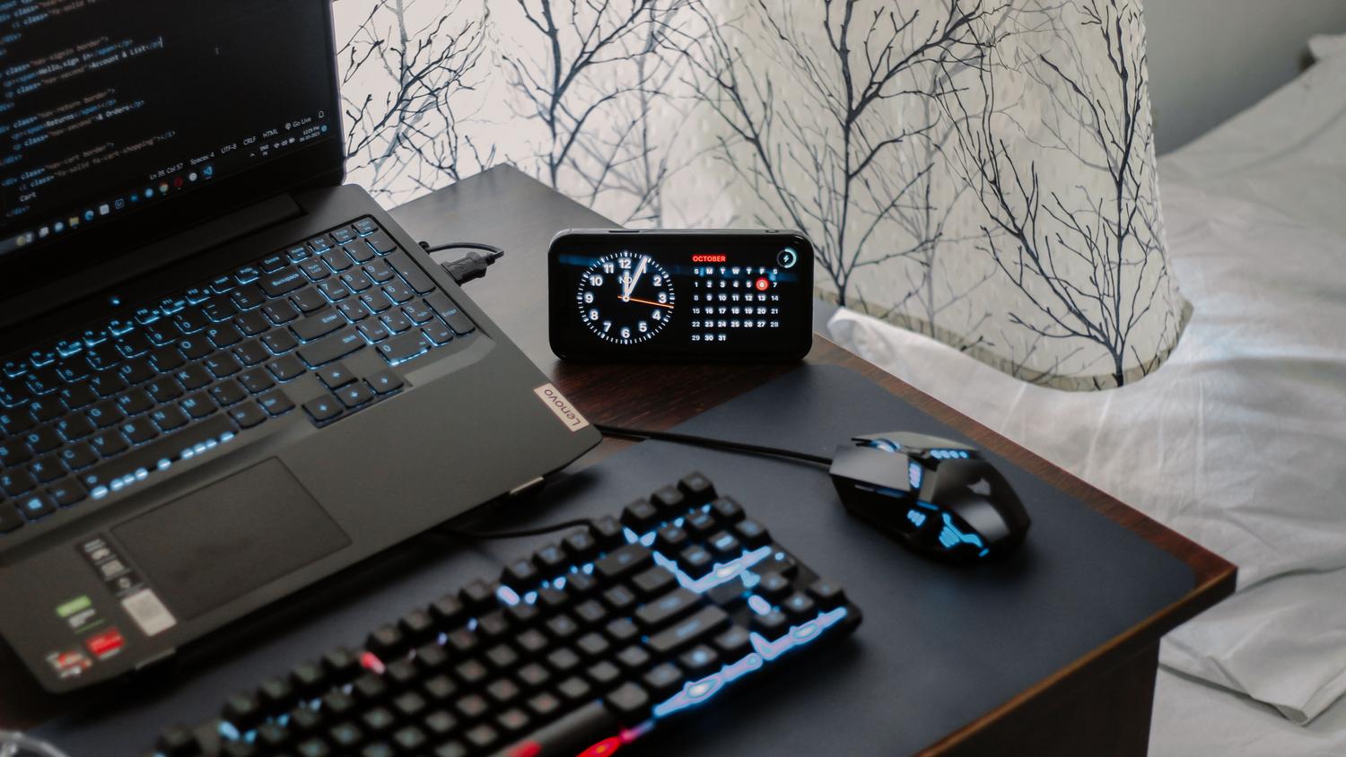 Espacio de trabajo tecnológico con un ordenador y un reloj digital, ilustrando la programación de tareas asíncronas.